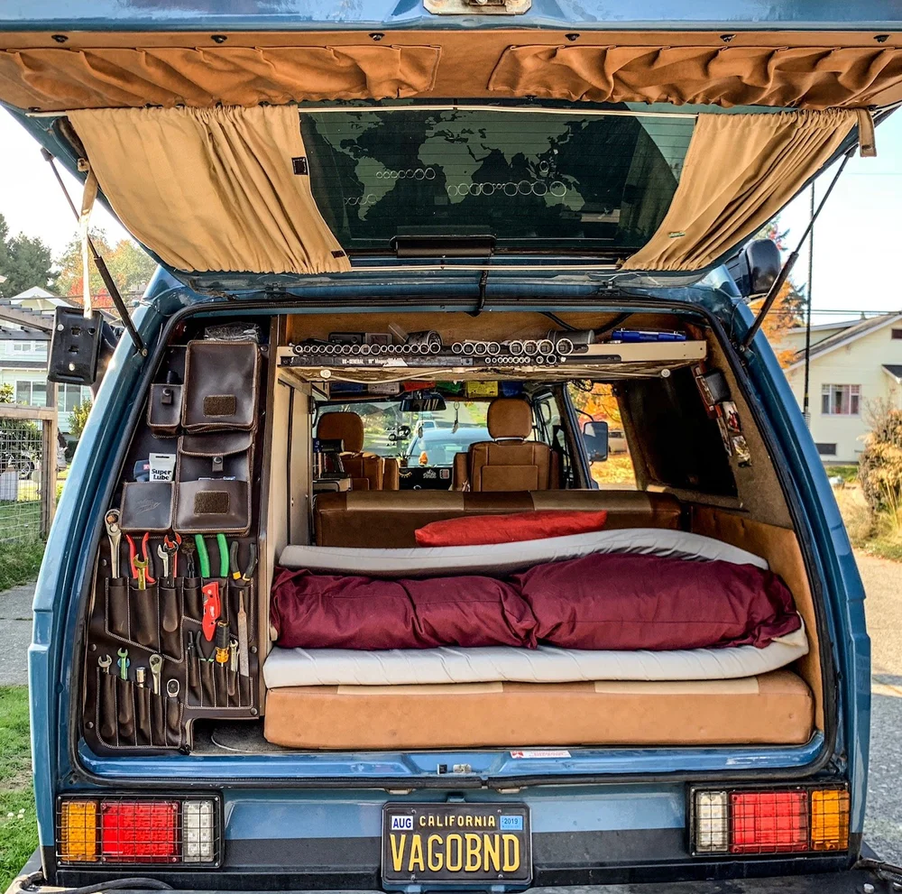 Westy Bravo leather tool organizer beside the rear bed of a blue Vanagon Westfalia with its hatch open
