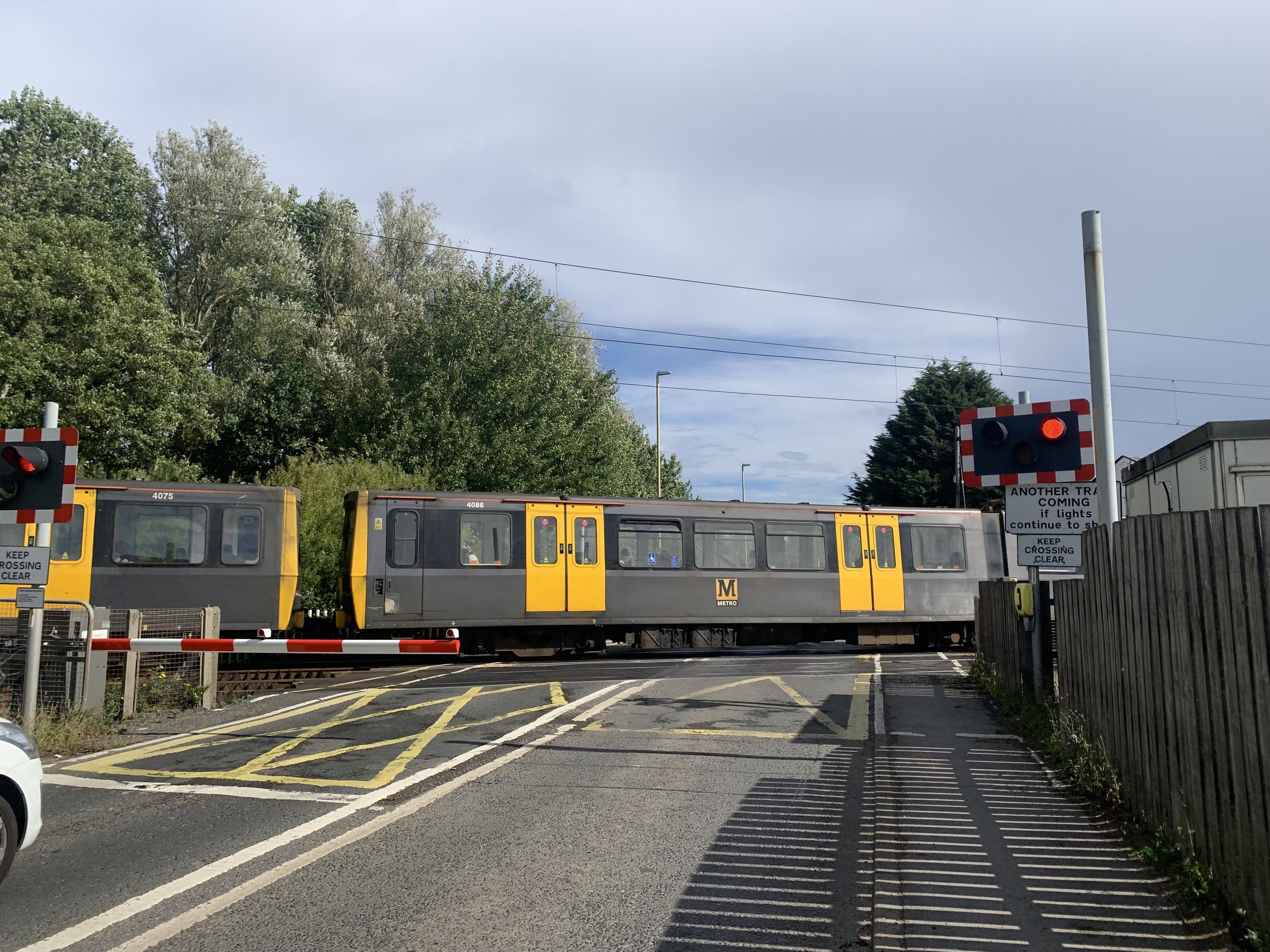 A train stopped at a crossing with red warning signals, trees in the background, and a cloudy sky overhead.