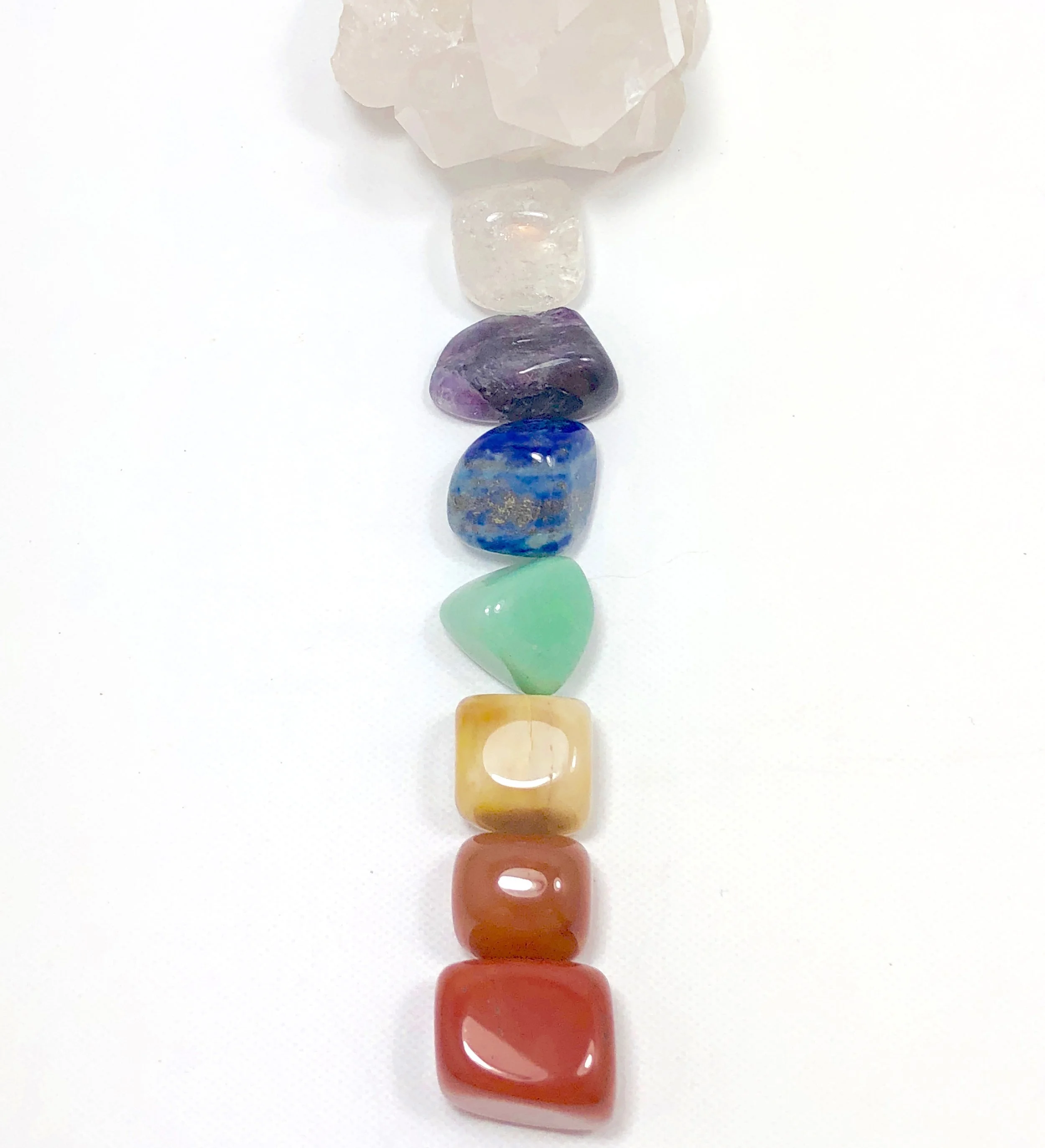 A vertical line of polished stones and shells in various colors, including white, purple, blue, green, yellow, and orange, arranged on a white background.