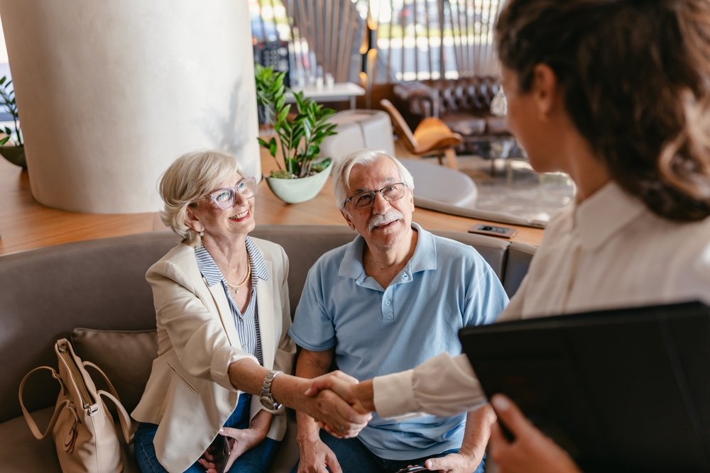 A smiling senior couple shaking hands with their Sunshine Legacy Concierge advocate during an initial family consultation