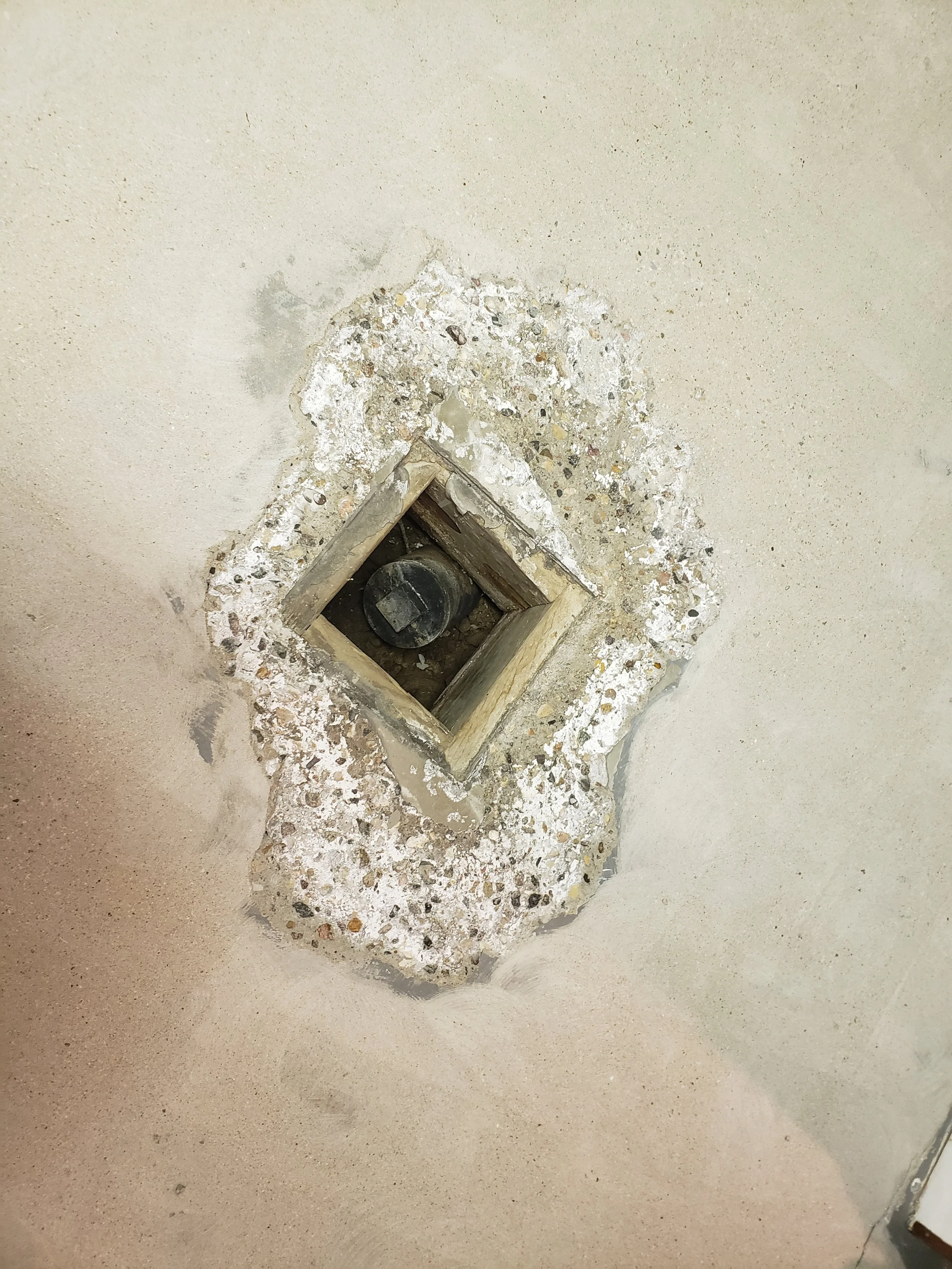 Close-up of basement drain surrounded by damaged and crumbling concrete with peeling paint and exposed debris.
