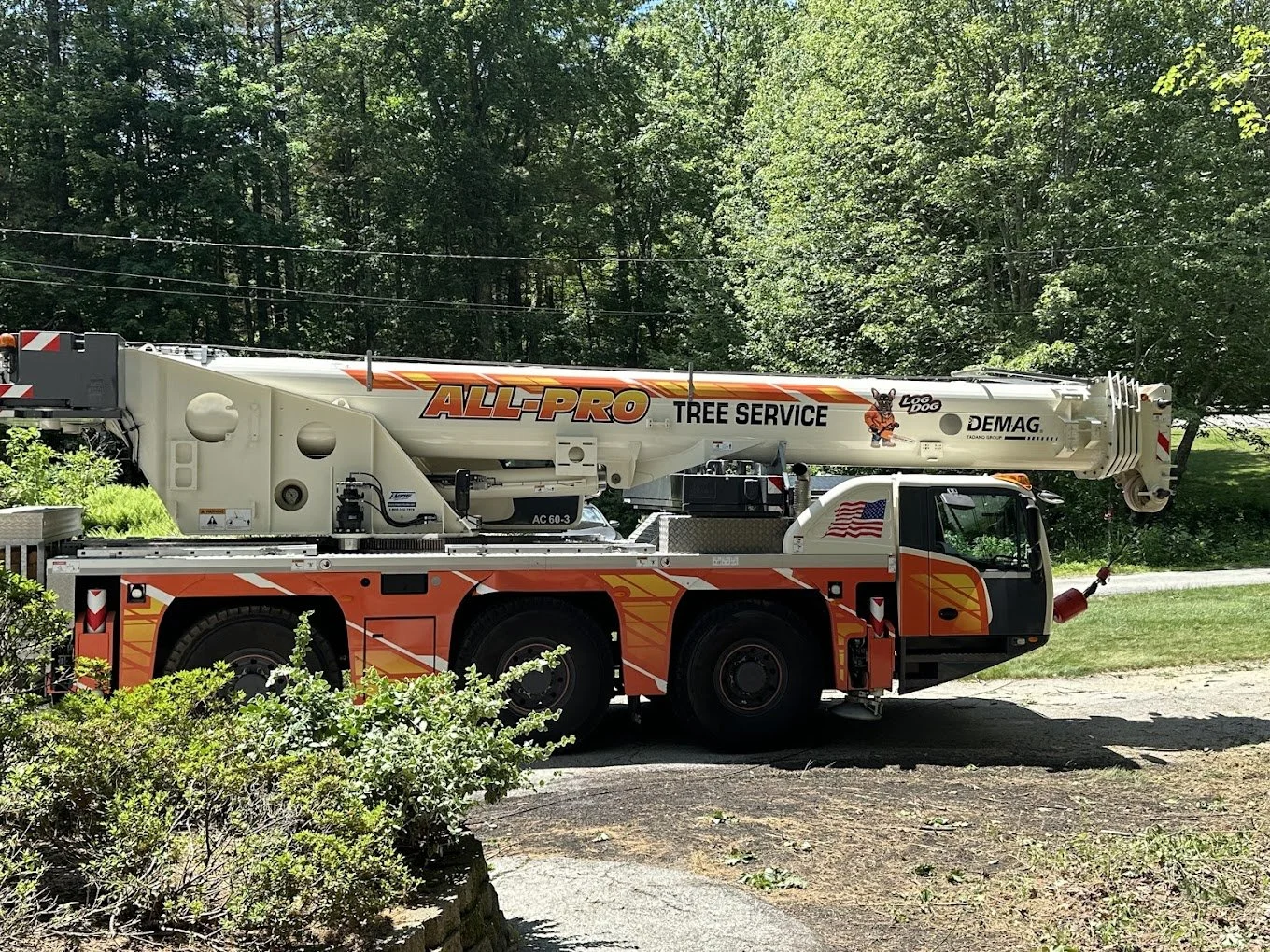A large orange and white tree service bucket truck parked on grass with trees in the background.