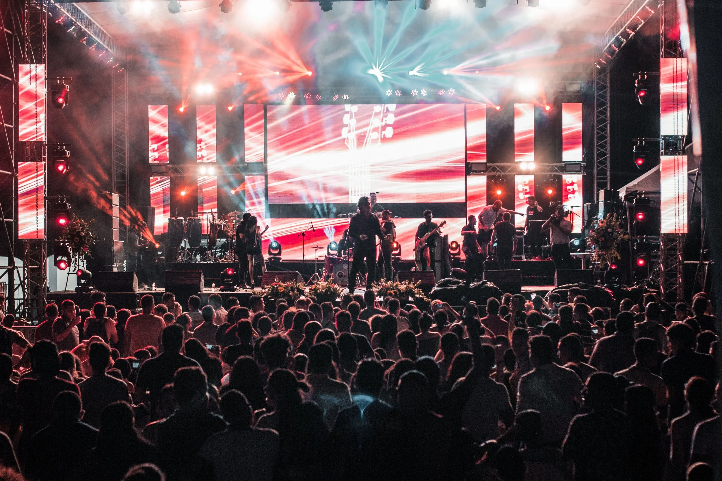 Stage with multiple performers and colorful lights, large crowd watching at a concert