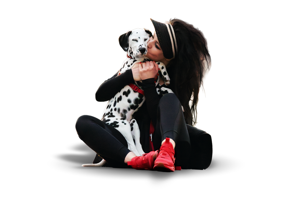 A woman in athletic wear and red sneakers sitting on the floor hugging a Dalmatian puppy, surrounded by a black background.