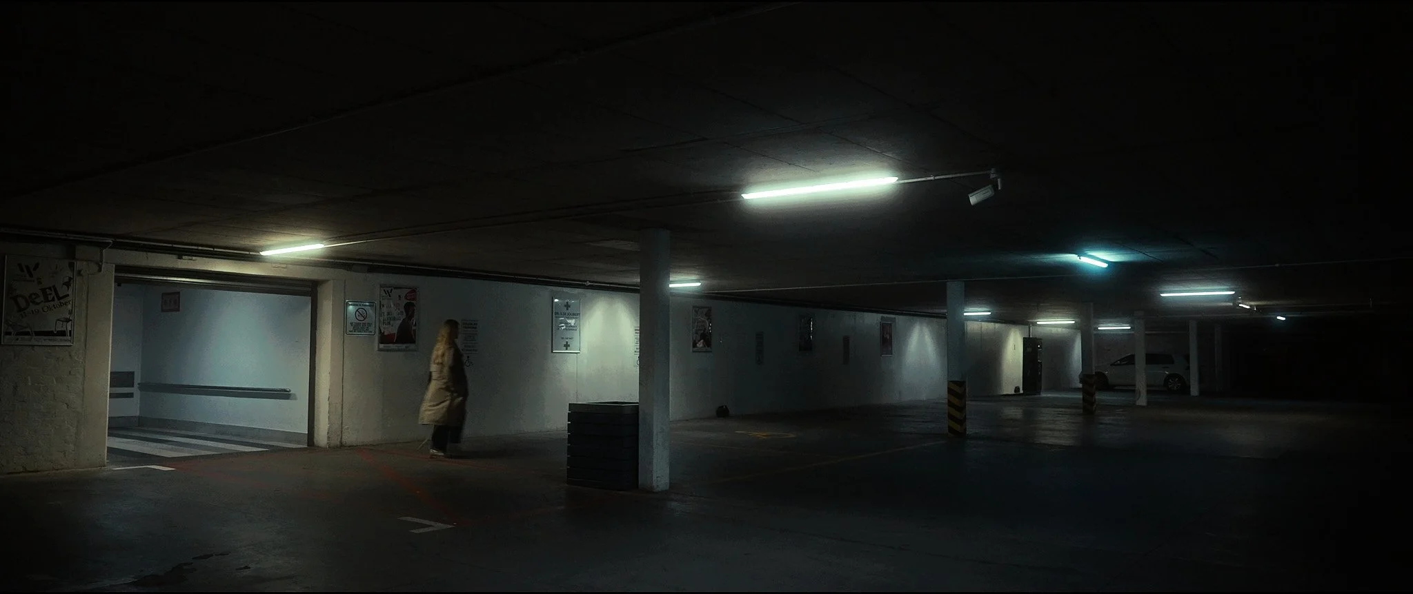 Underground parking garage with dim lighting, a person walking, and a few parked cars.