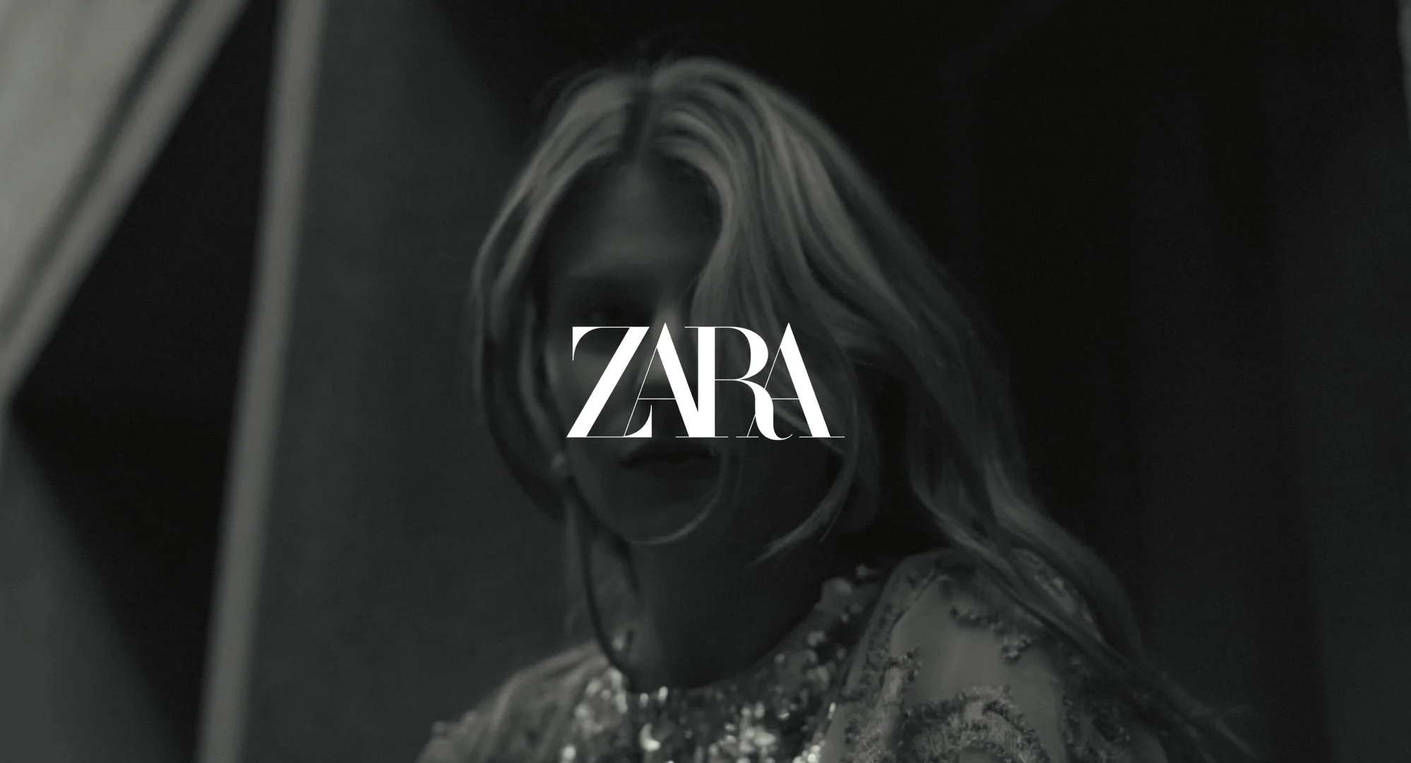 Black and white image of a woman with long hair, and a necklace, with the Zara logo in the center.