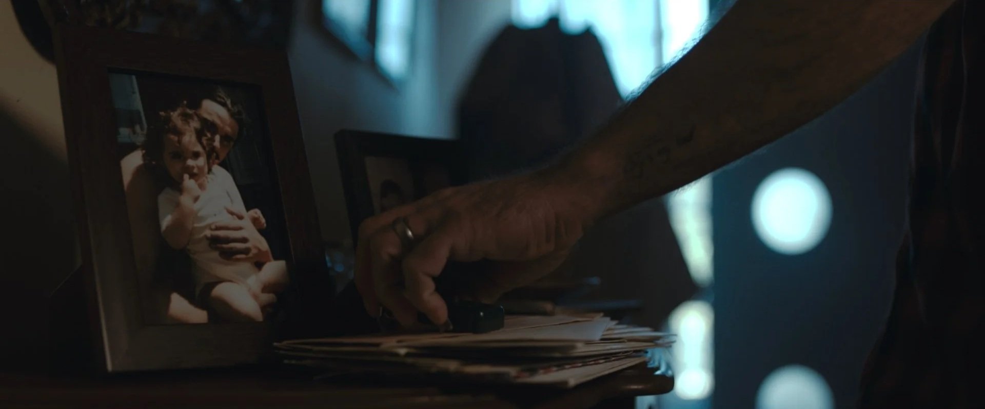 A person's hand reaching for papers on a table, with a framed photo of a young girl in the background.