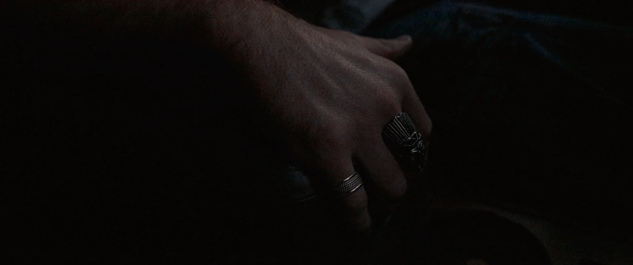 Close-up of a person's hand wearing rings, resting in a dark setting.