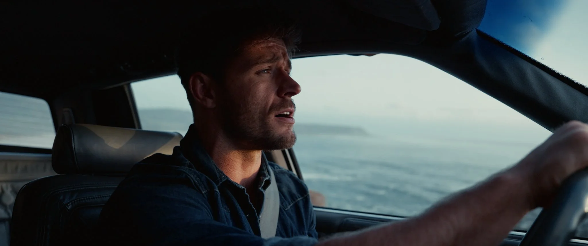 Man driving a car along the coastline during the day.