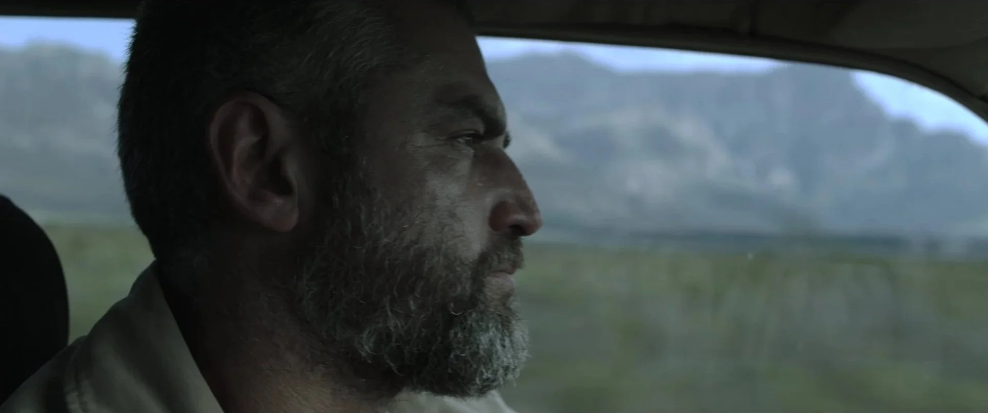 Close-up of a man with a beard driving a vehicle through a rural landscape.