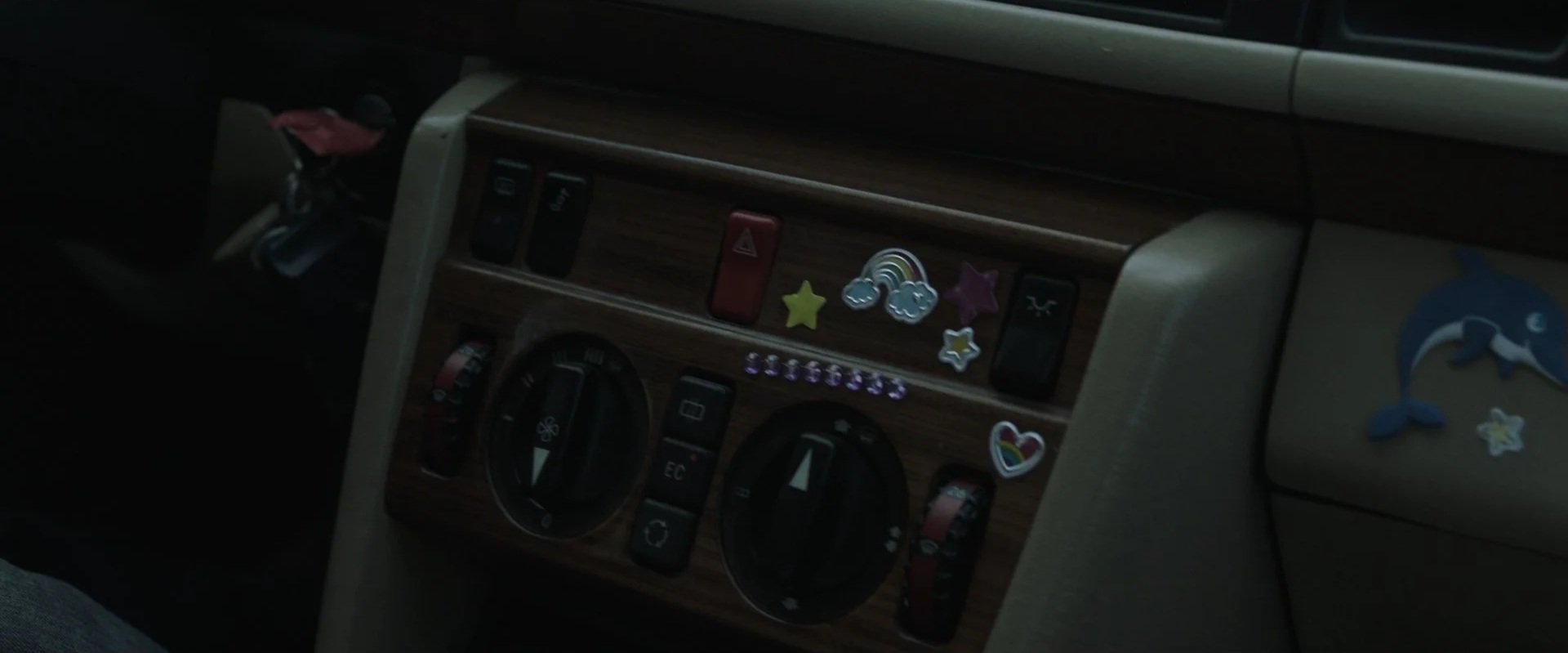 Close-up of a car dashboard with colorful stickers, including stars, clouds, a rainbow, and a dolphin, on the wooden panel and side panel.