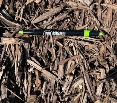 A black and green Nickel Venture pen resting on wood chips or mulch.
