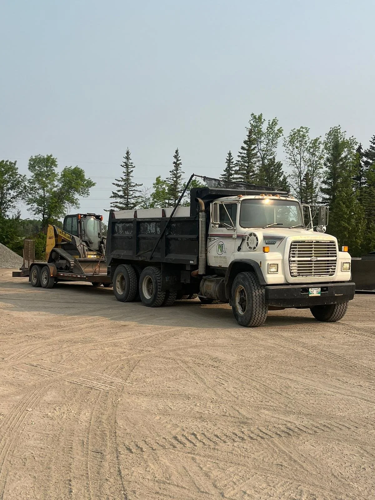 A white truck hauling a skidsteer.