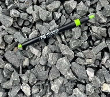 A black and green pen lying on gray gravel rocks.