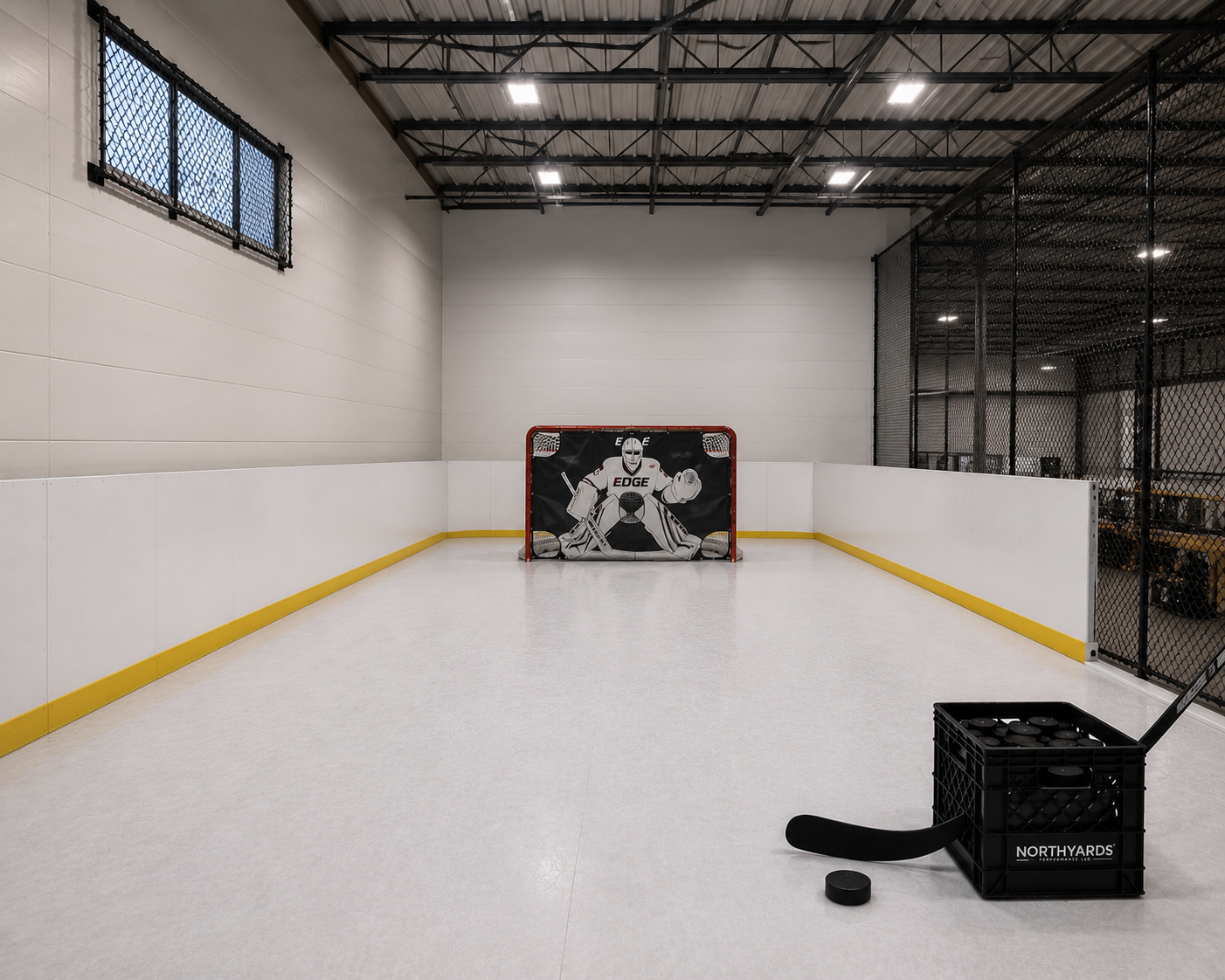 Indoor hockey rink with a goaltender net, hockey puck basket, and hockey equipment.