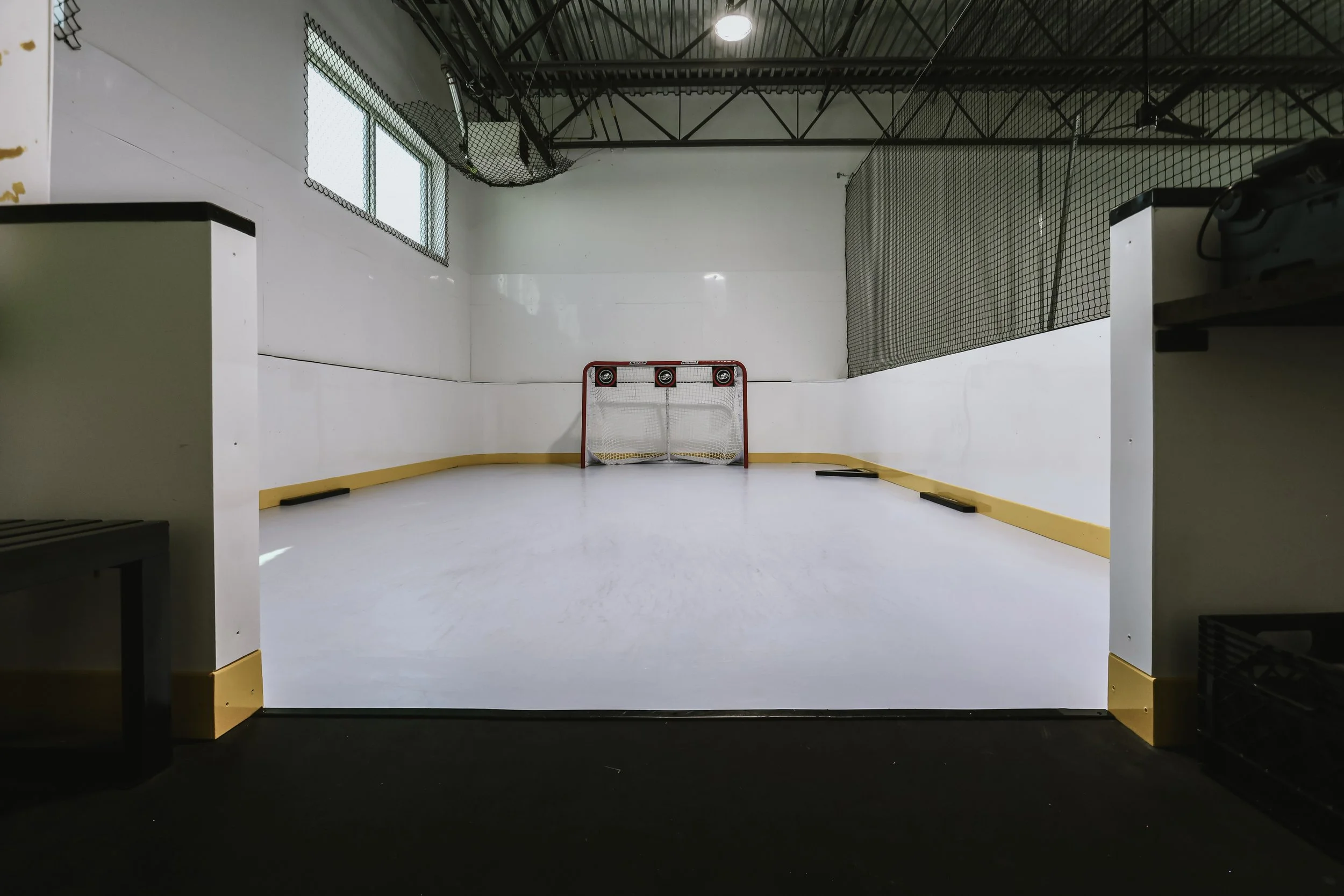 Indoor hockey rink with a goaltender net, hockey puck basket, and hockey equipment.