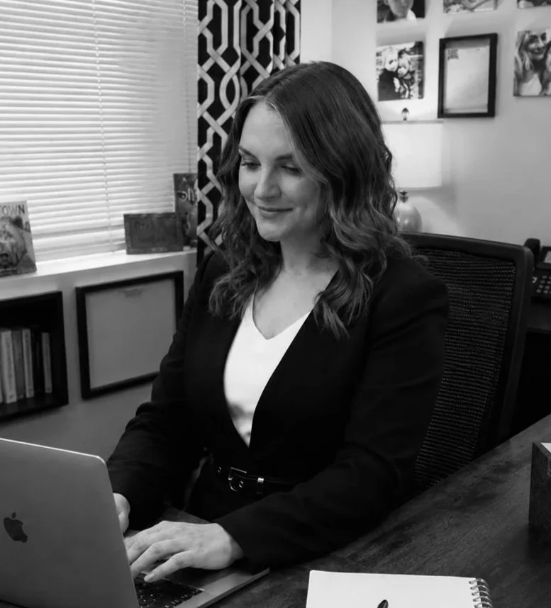 A woman with wavy hair working on a laptop in an office setting.
