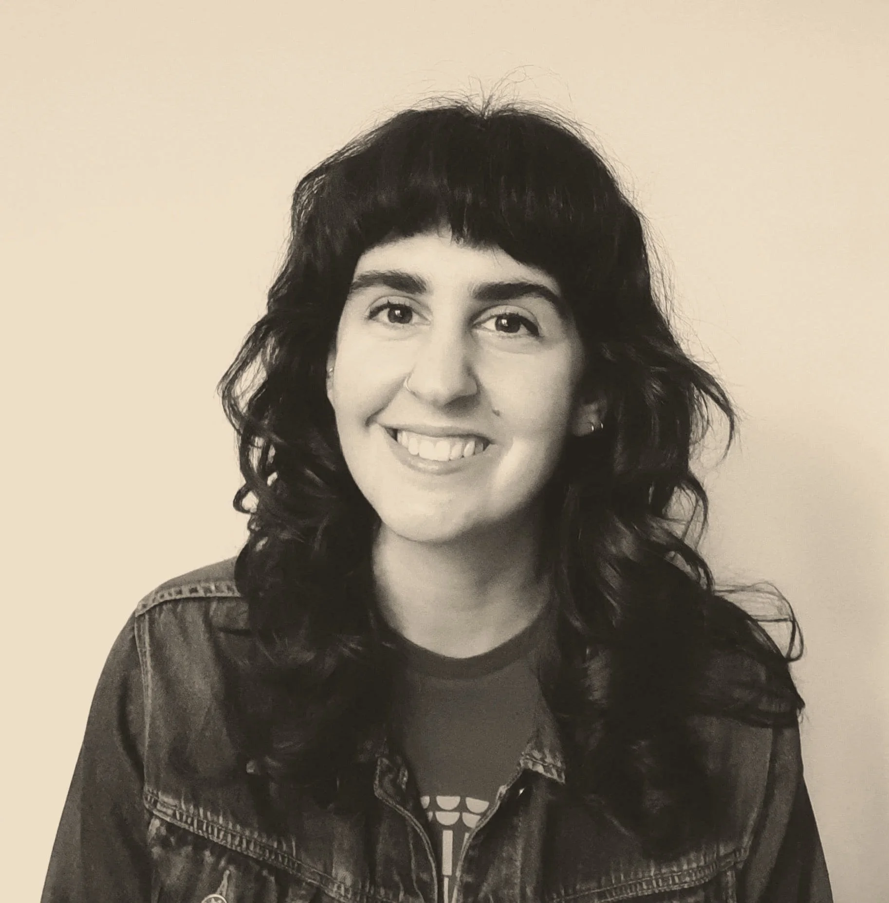 Black and white photo of a smiling woman with curly hair wearing a jacket with a sun graphic on the shirt underneath, against a plain background.