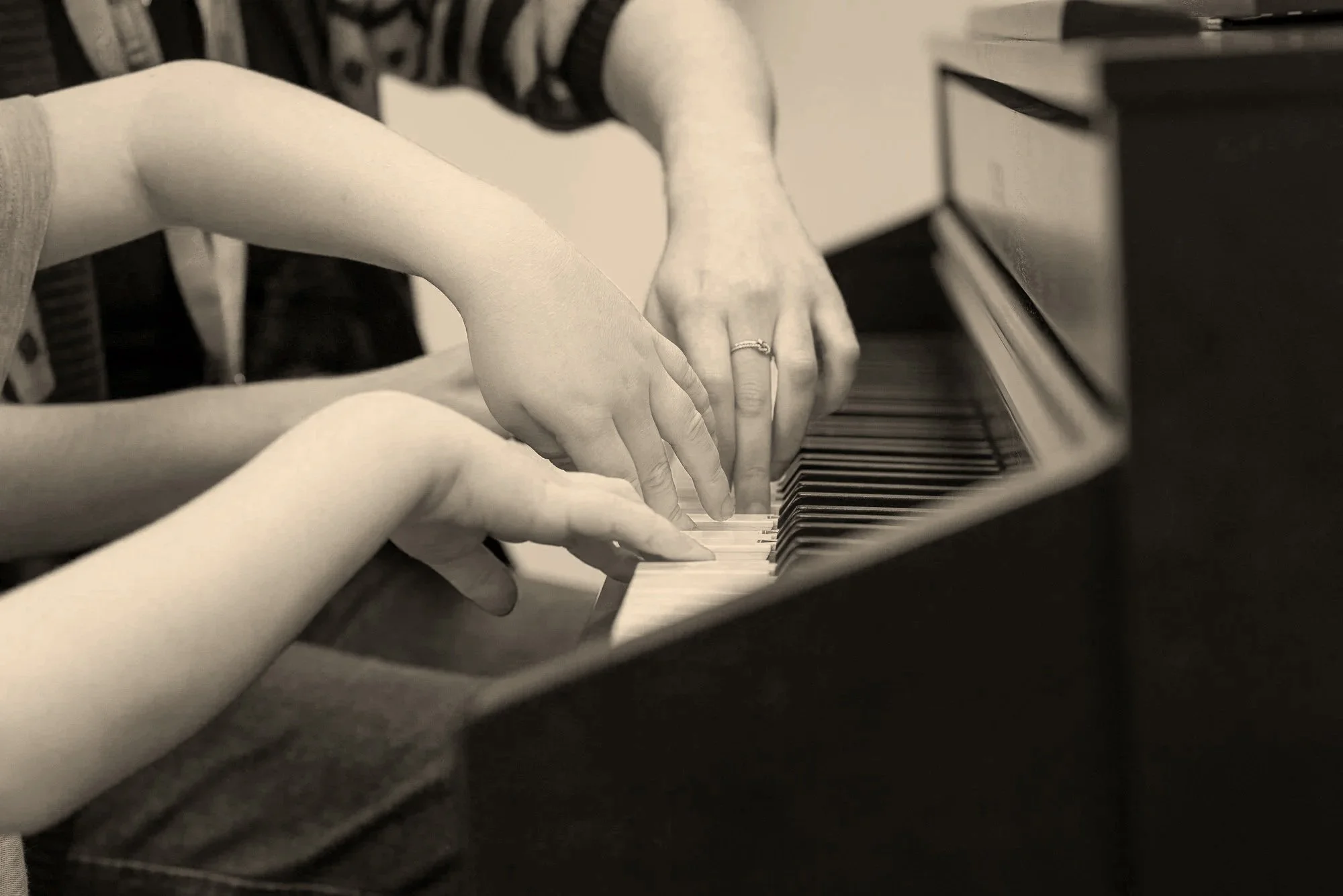 Black and white photo of hands playing a piano keyboard.