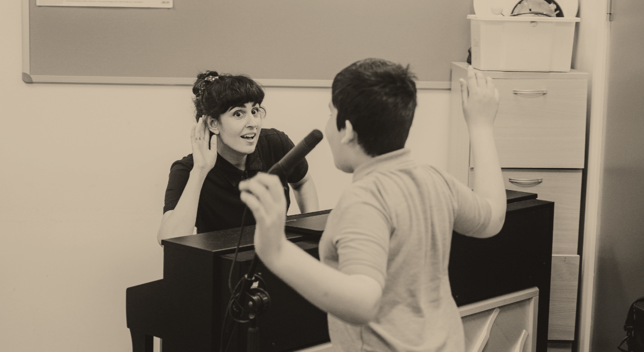 A woman at the piano and a boy at the microphone engaged in music making together.