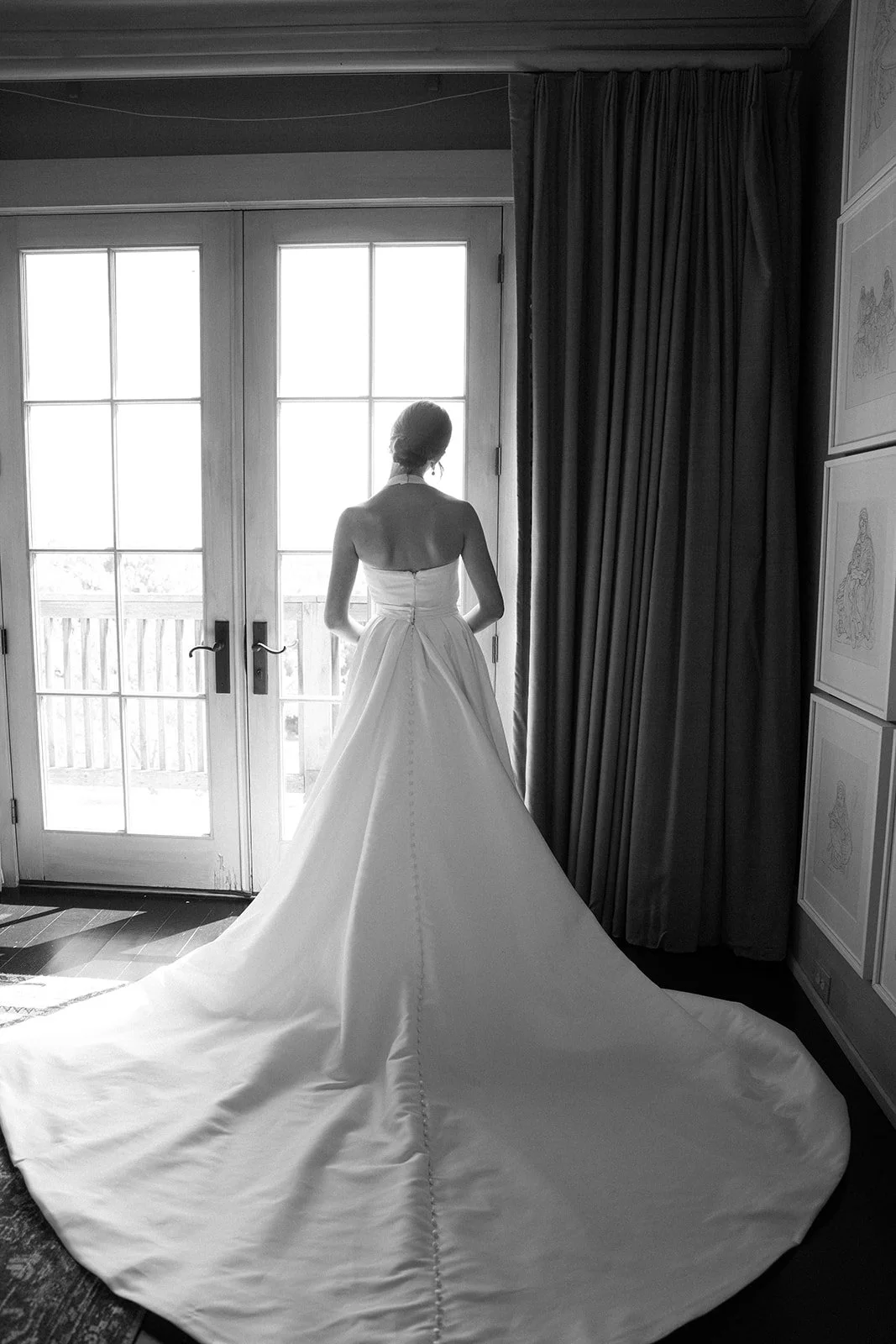 A woman in a wedding dress standing in front of glass doors, looking outside, with a long train on the floor.