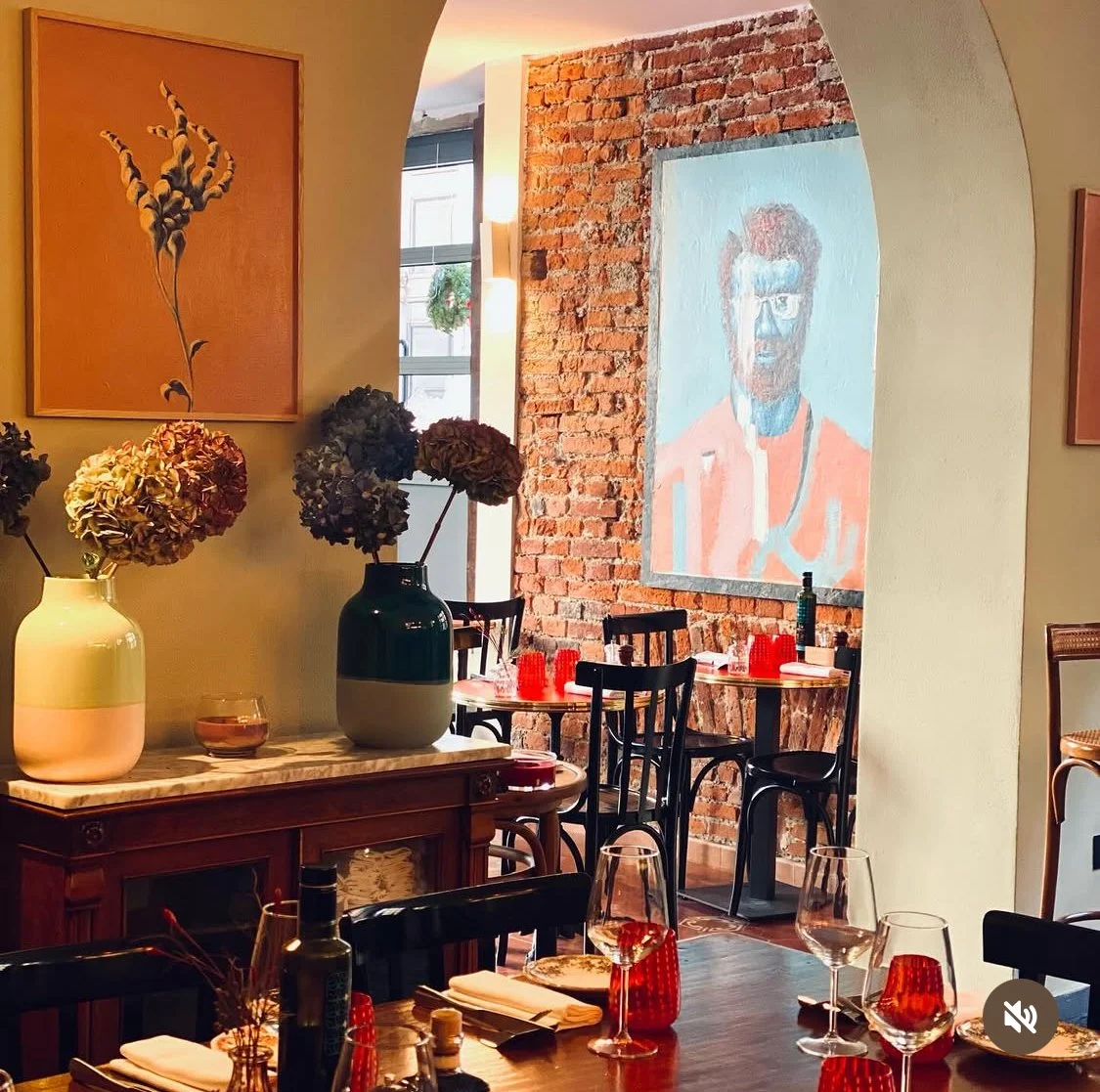 Sala del ristorante con tavoli apparecchiati, mattoni a vista e opere d'arte
