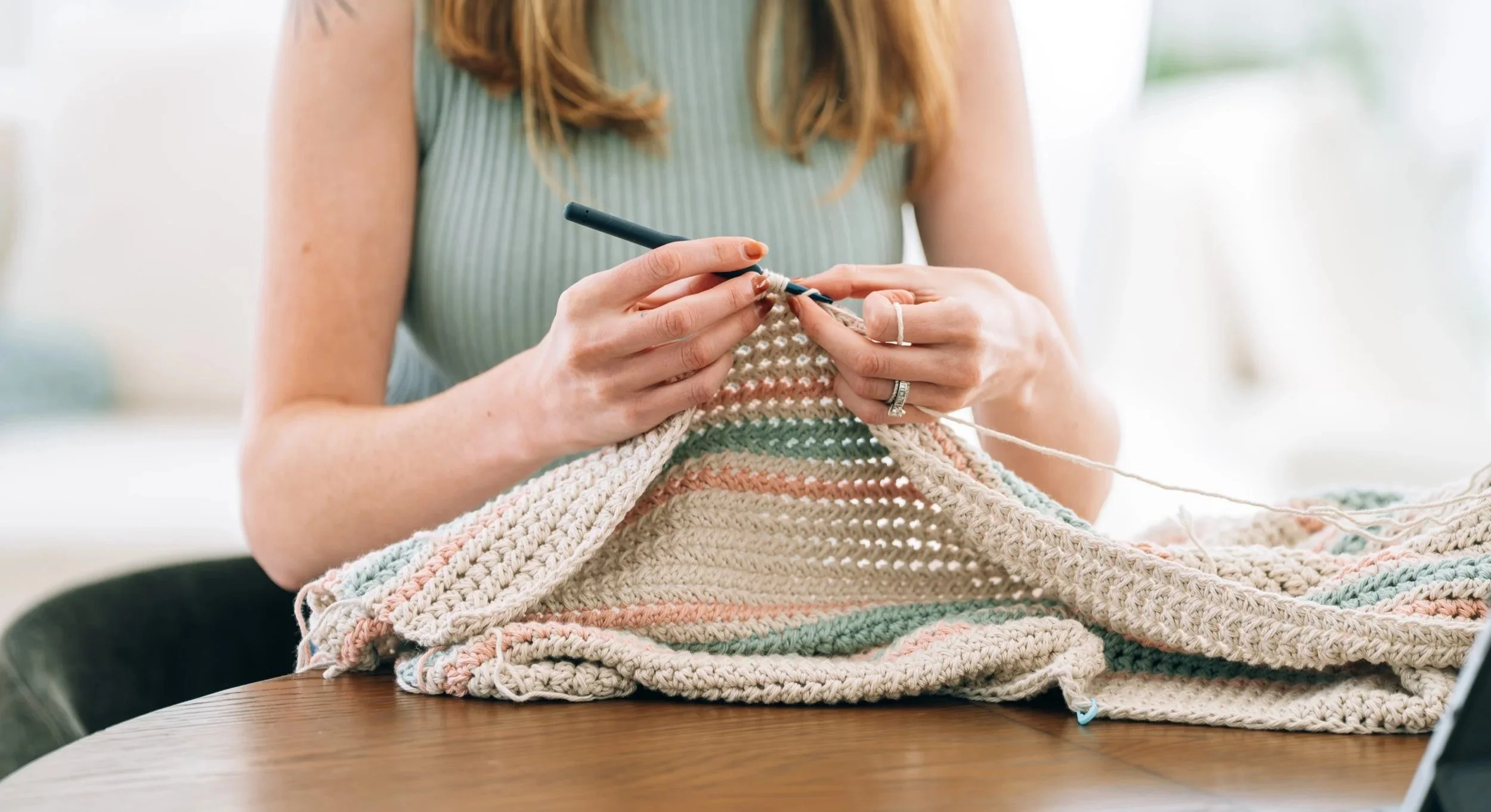 Person knitting a colorful striped blanket with a crochet hook.
