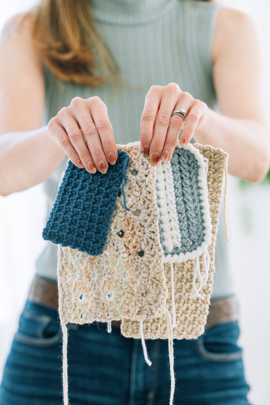 Person holding up several colorful knitted and crocheted fabric samples
