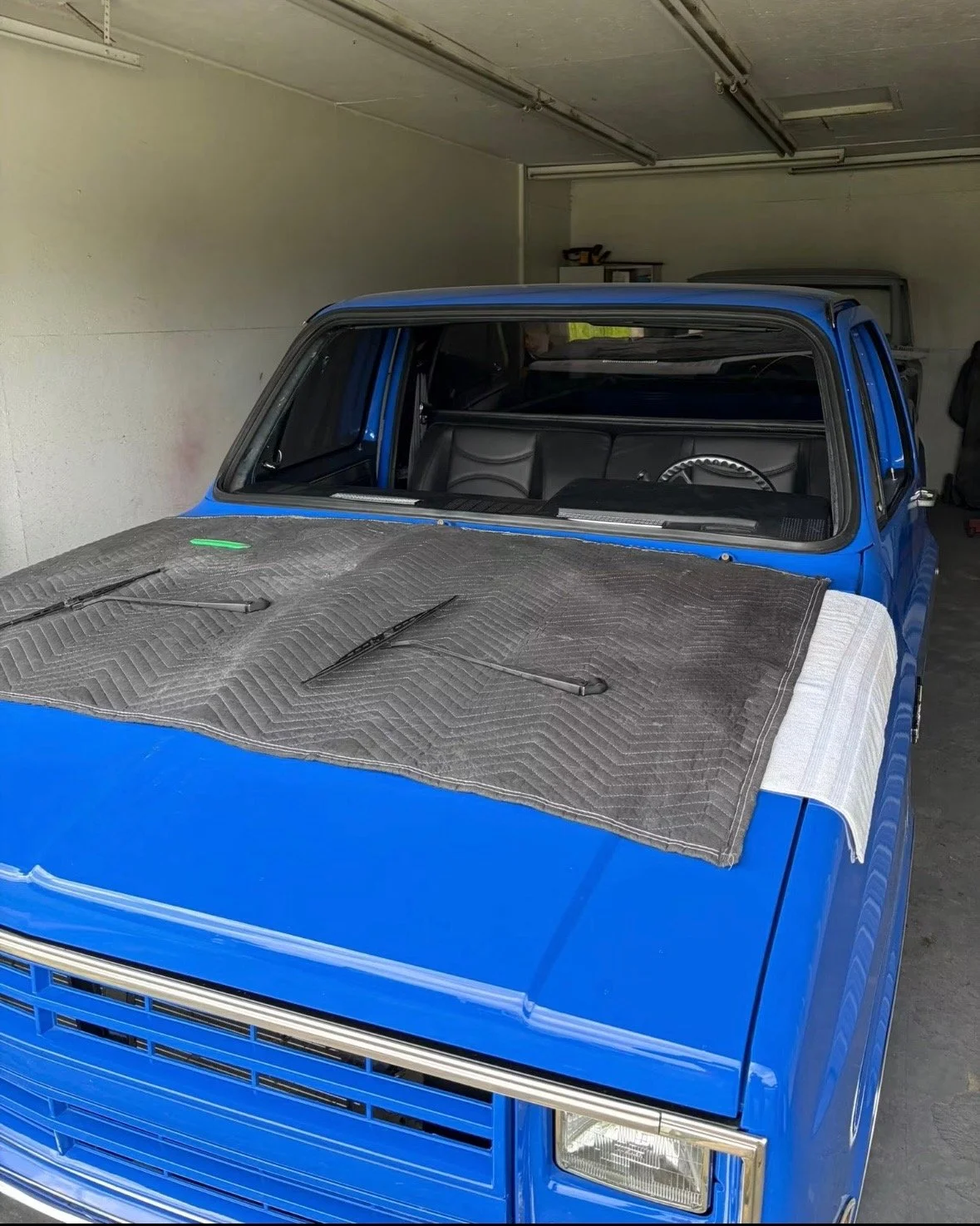 Blue vintage vehicle in a garage with a protective covering on the hood and windshield wipers.