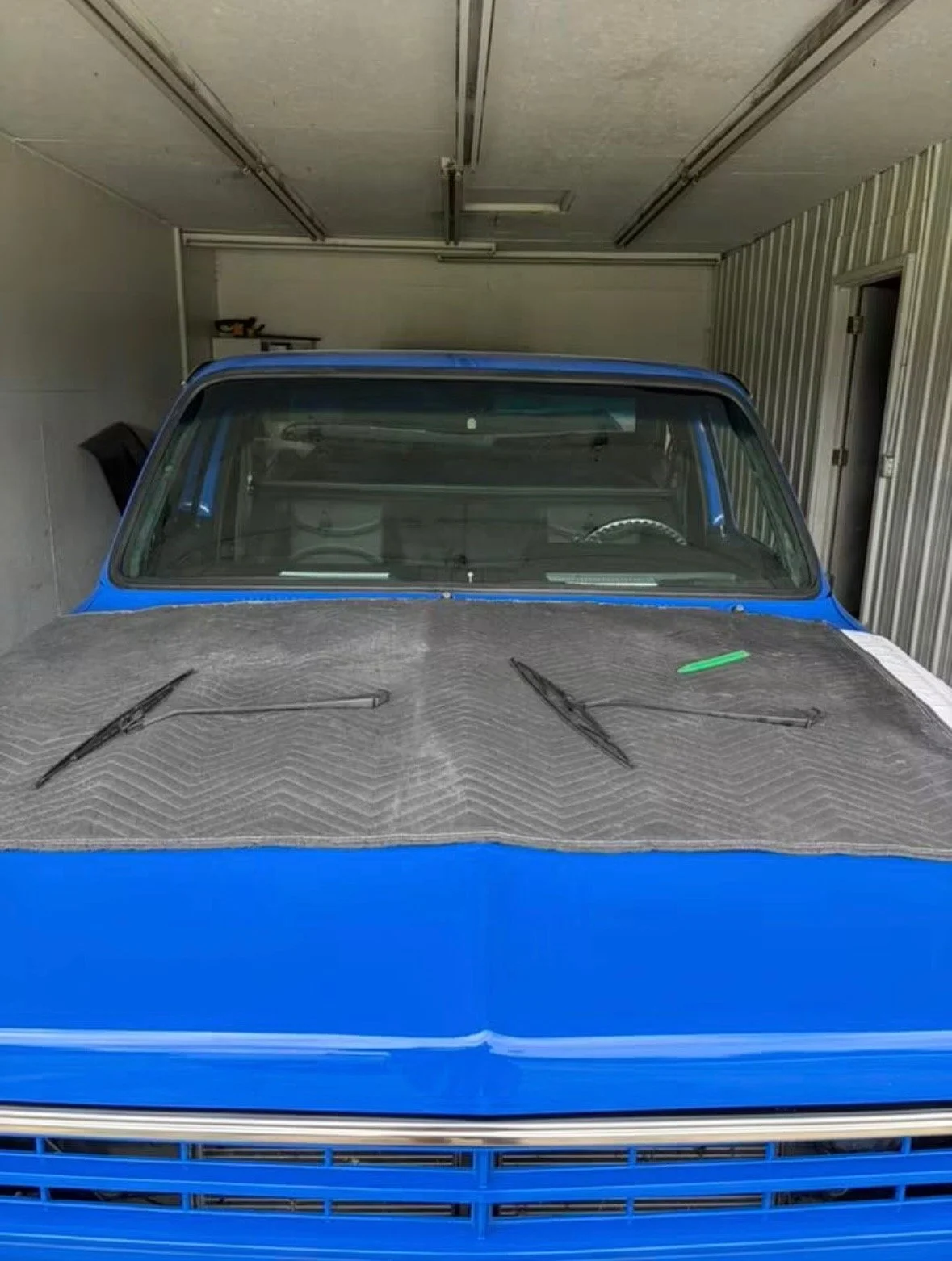 Front view of a blue car in a garage with a dust cover and windshield wipers on the hood.
