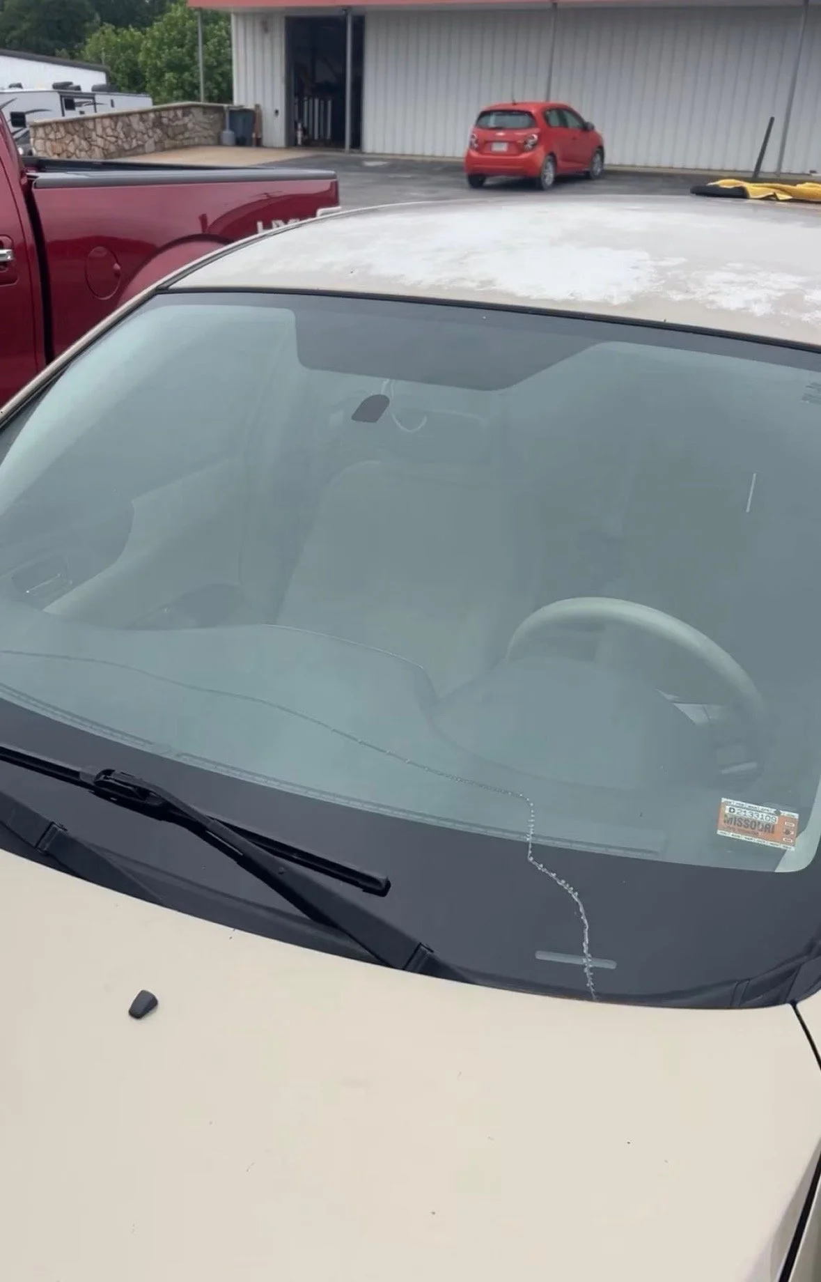 Front windshield of a vehicle with a Missouri parking permit sticker, cracked windshield, and a crack running from the bottom to the middle.