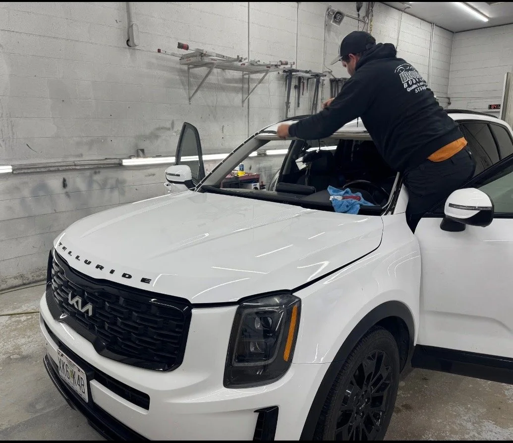 A person working on the interior of a white SUV inside a garage or workshop. The individual appears to be installing or repairing something in the vehicle.