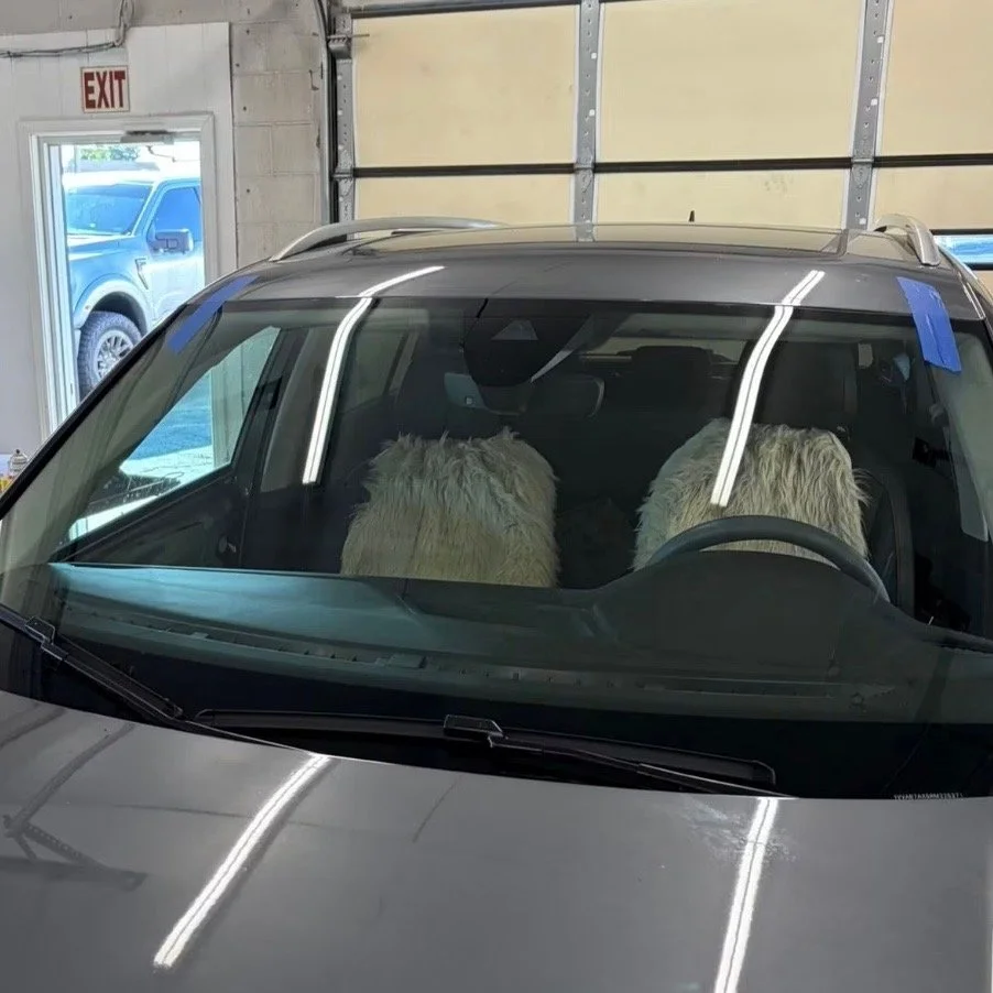 Front view of a car with two large fluffy dog beds on the front seats, viewed inside a garage or workshop.