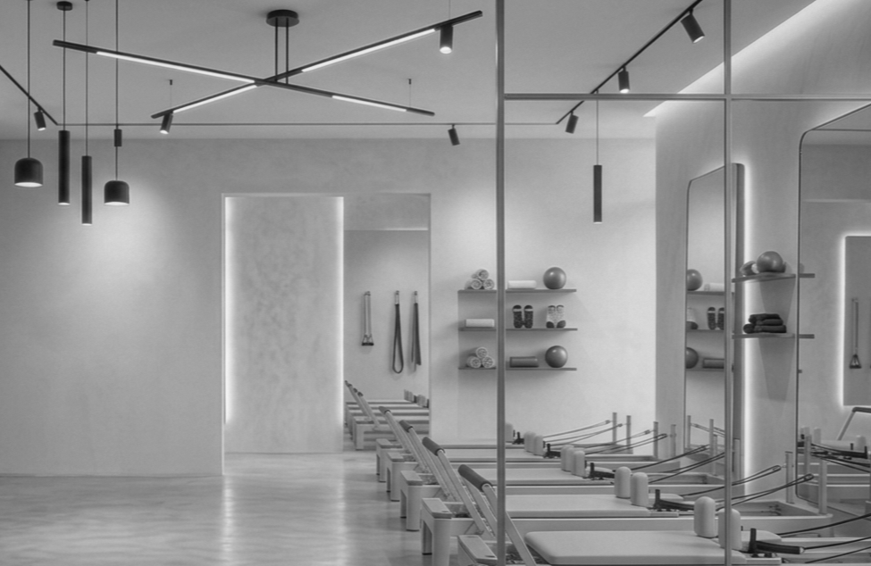 A modern Pilates or fitness studio with Pilates reformer machines, shelves with exercise balls and towels, and minimalist lighting fixtures.