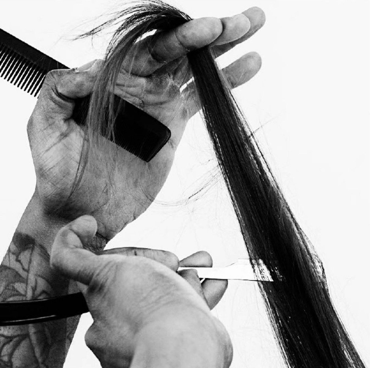 Black and white photo of a hairdresser's hand holding a section of long, straight hair with a comb, preparing for a haircut or styling.