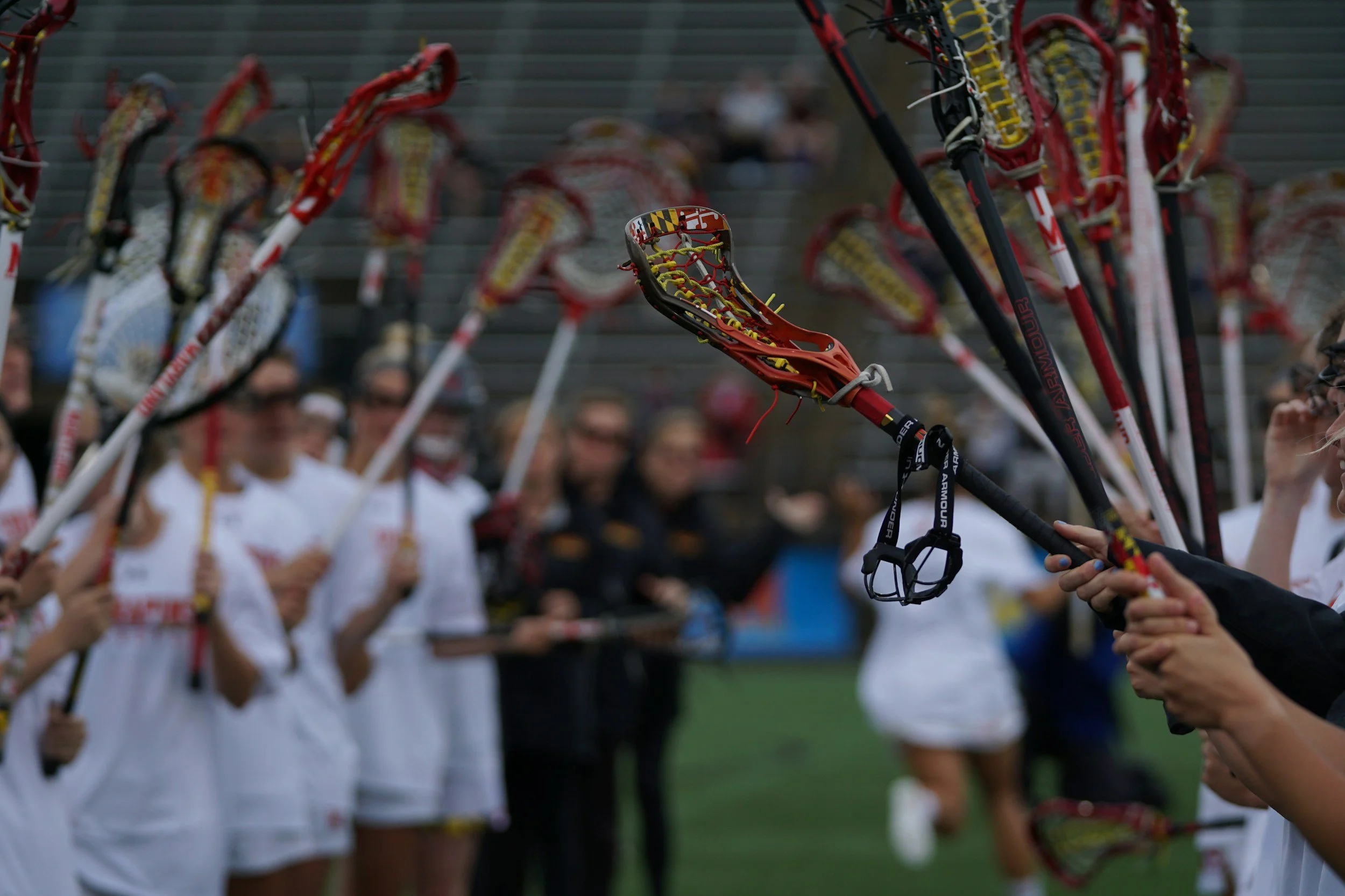 A group of people in white shirts holding lacrosse sticks during a game or practice on a field.
