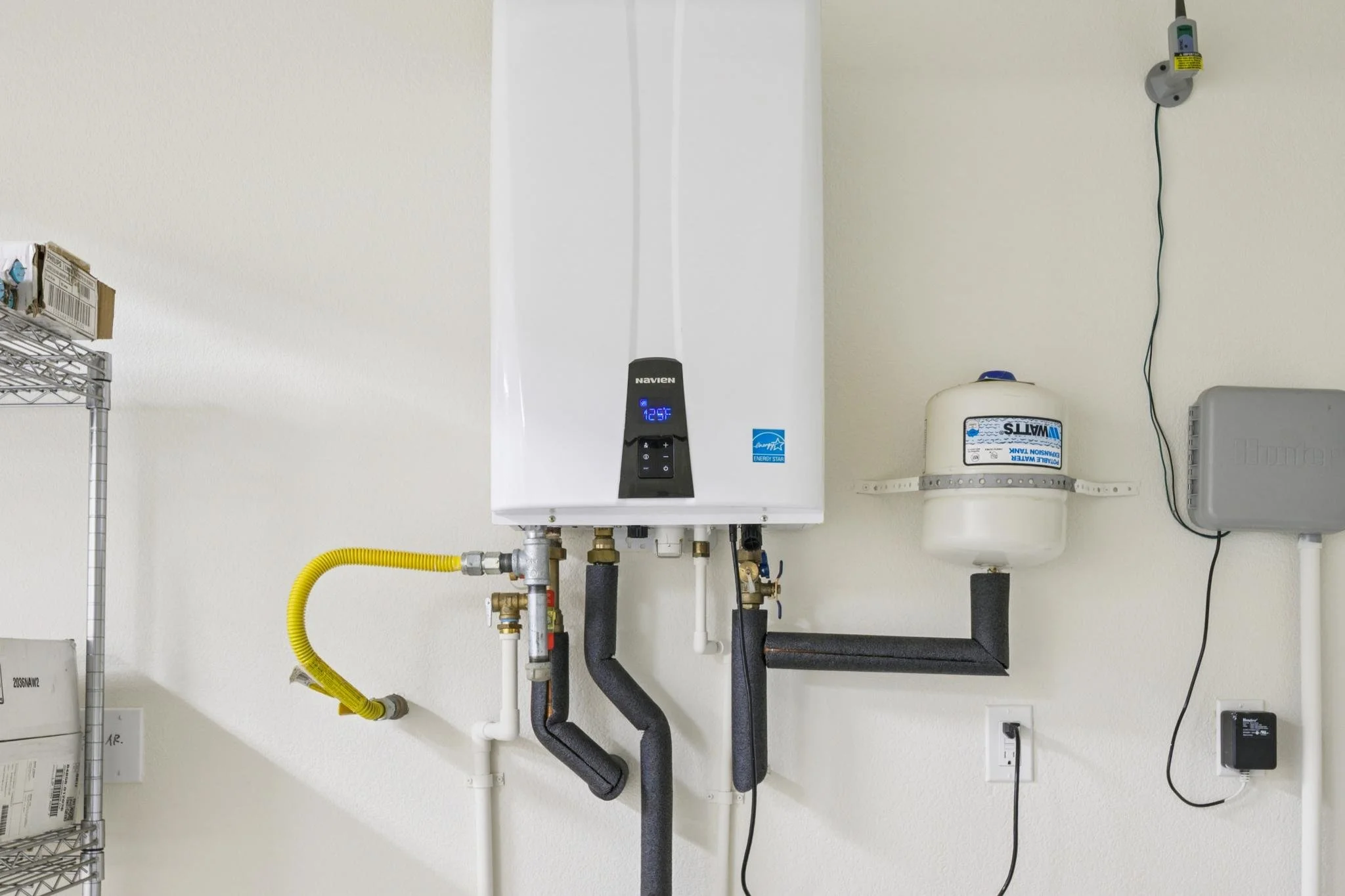 A utility wall with a white water heater, pipes, and electrical components, including a digital display on the water heater showing 125°F.