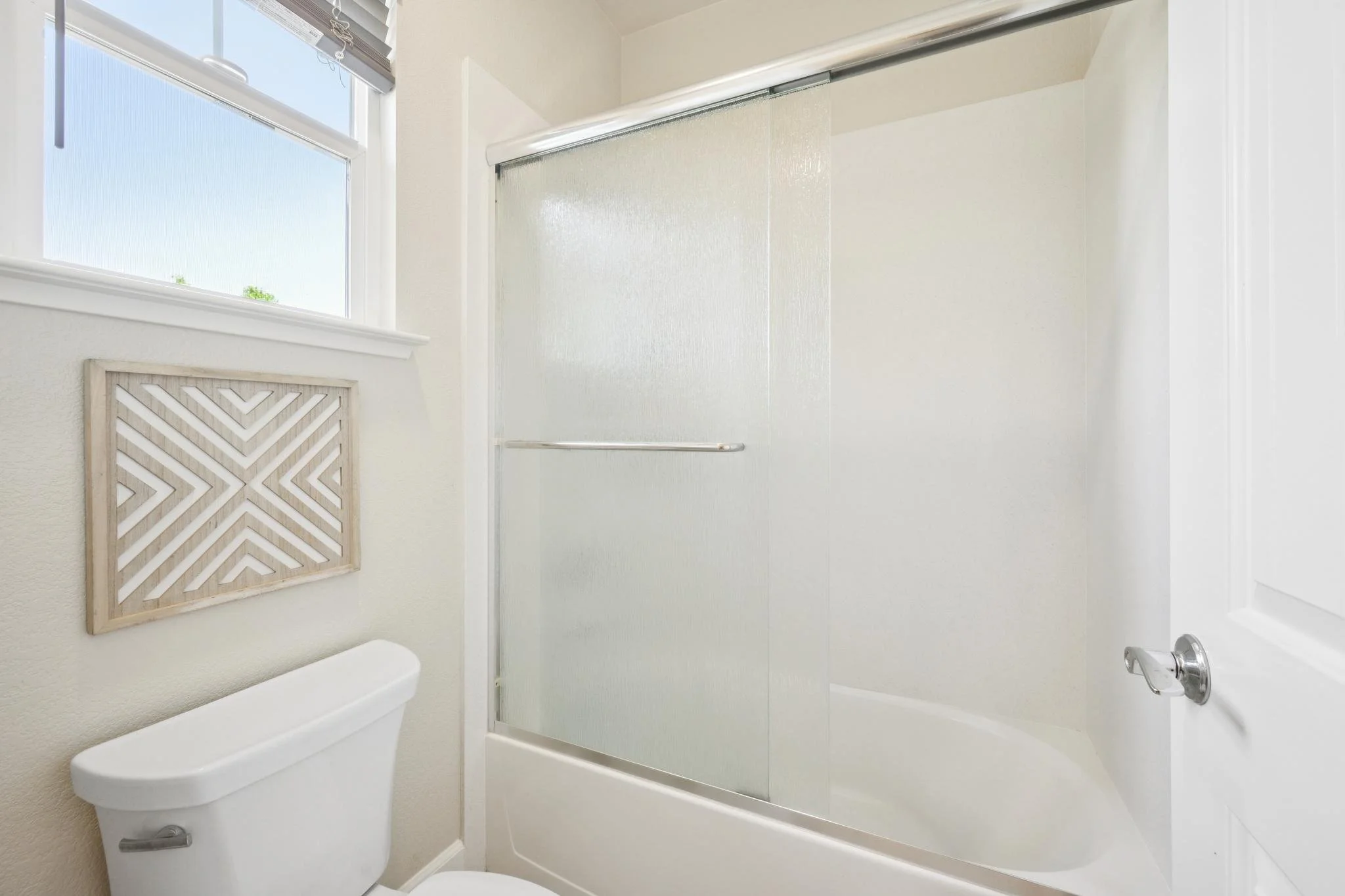 Bathroom with a white toilet, decorative wall panel, window, and shower with glass door.