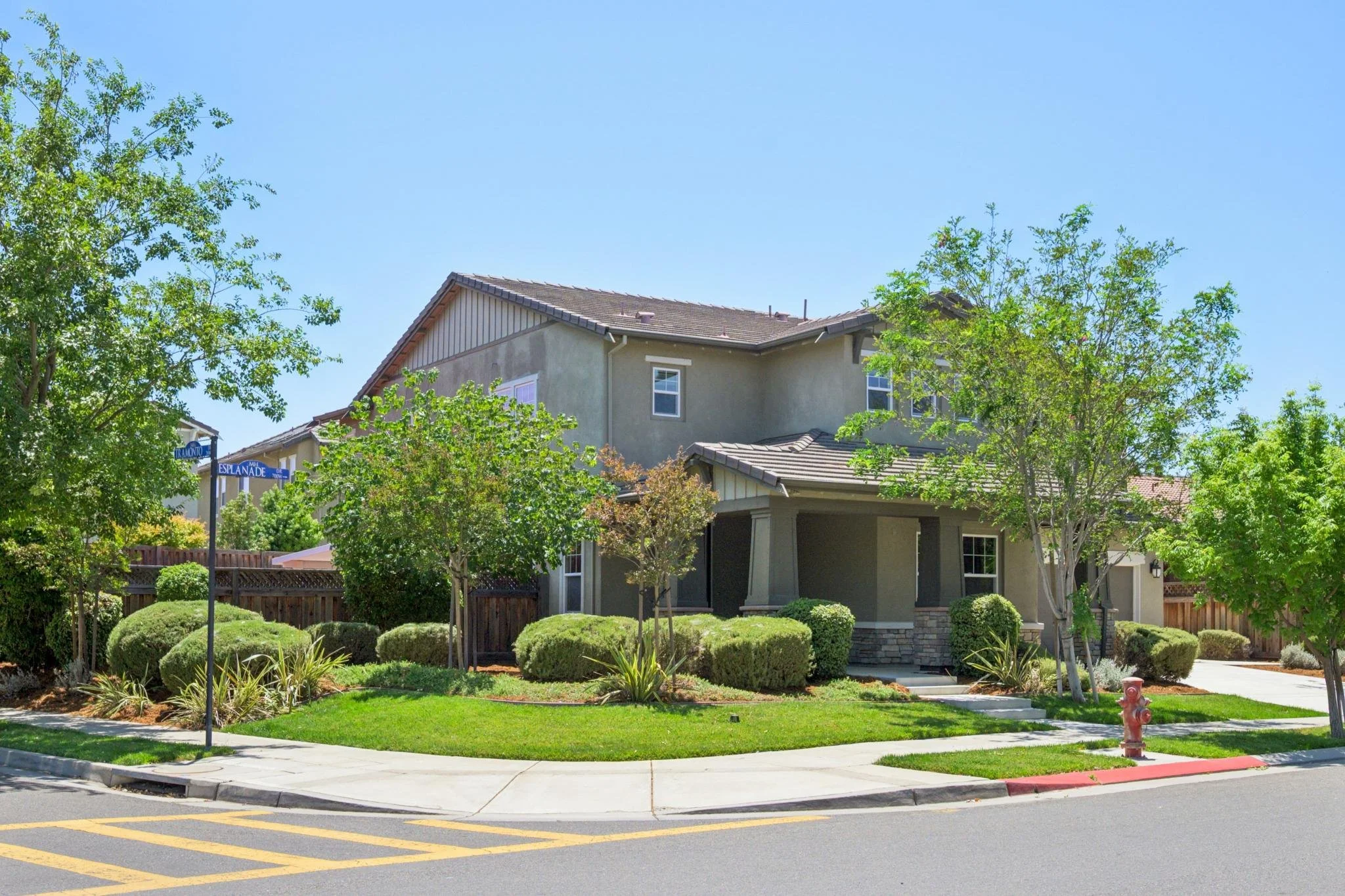 A two-story house with a landscaped front yard and trees, located at a street corner with a fire hydrant and sidewalk.