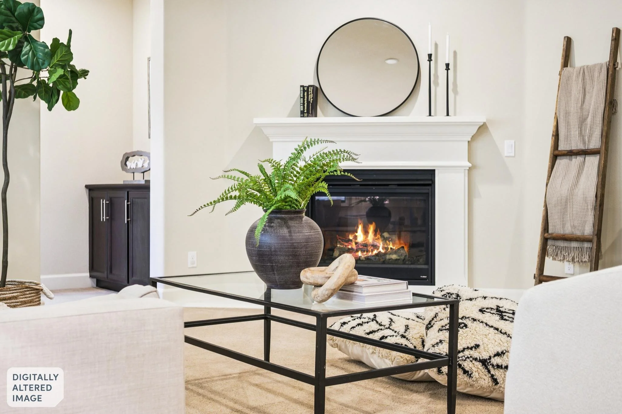 Living room with a fireplace, large mirror above mantel, black candlesticks, books, a potted fern on a glass coffee table, a beige and black rug, a dark cabinet, a ladder with blanket, and greenery in the corner.
