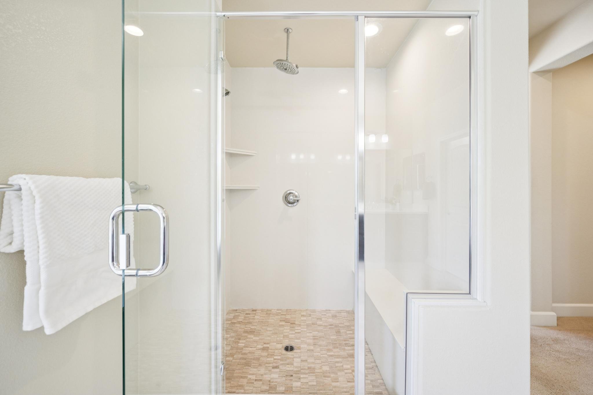 A walk-in shower with glass doors, a mounted shower head, and a built-in shelf. A white towel hangs on a towel bar outside the shower.