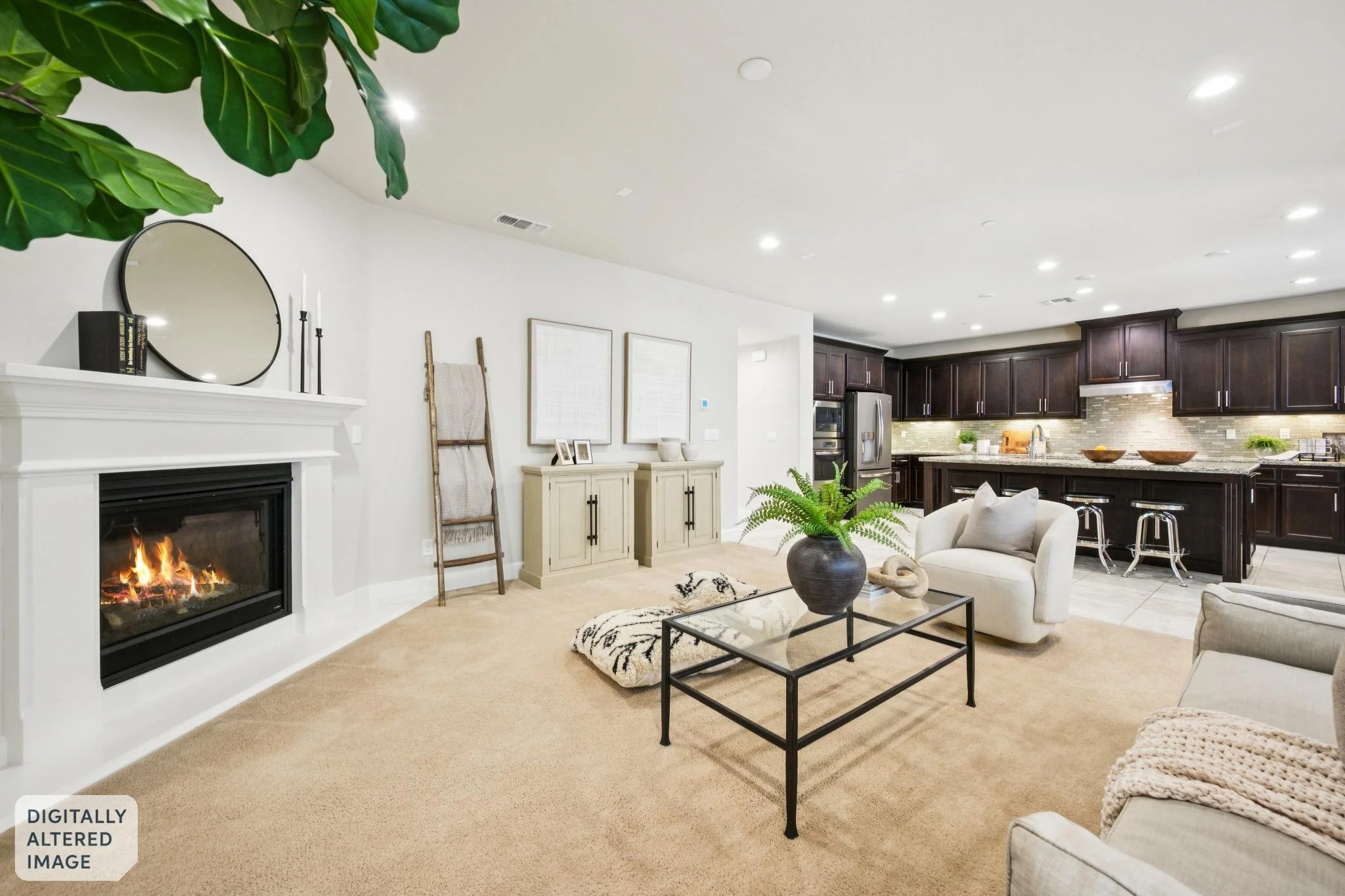 Open-concept living room with a beige carpet, white walls, and a fireplace. The room features a white armchair, a black metal coffee table with a decorative black vase and a carved wooden figure, and a beige rug. In the background, there are dark woo