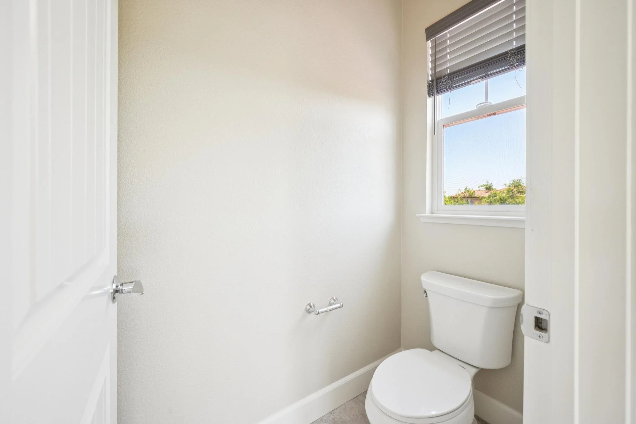 Small bathroom with a toilet, a window with blinds, white walls, and minimal decor.