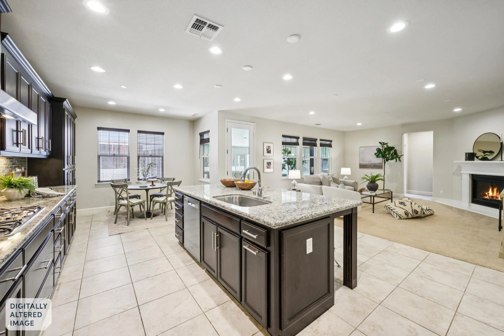 Open-concept kitchen and living room with granite island, dark wood cabinets, dining area, large windows, fireplace, and comfortable seating.