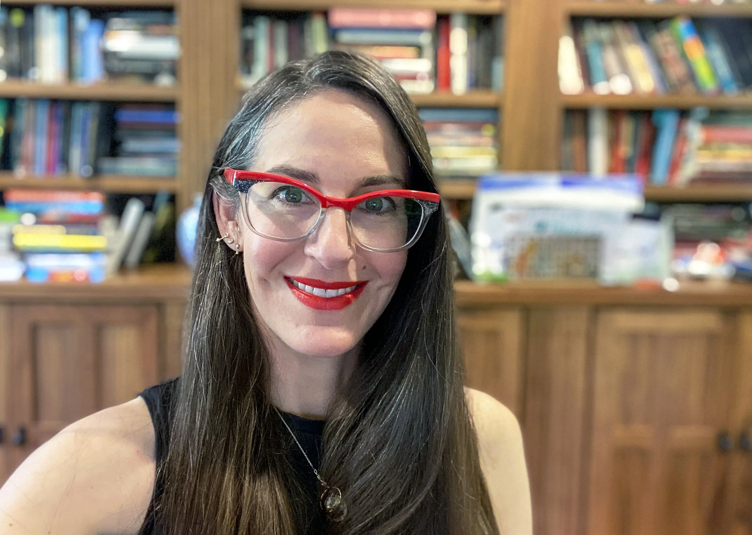 A woman with dark hair and read glasses smiles at the camera
