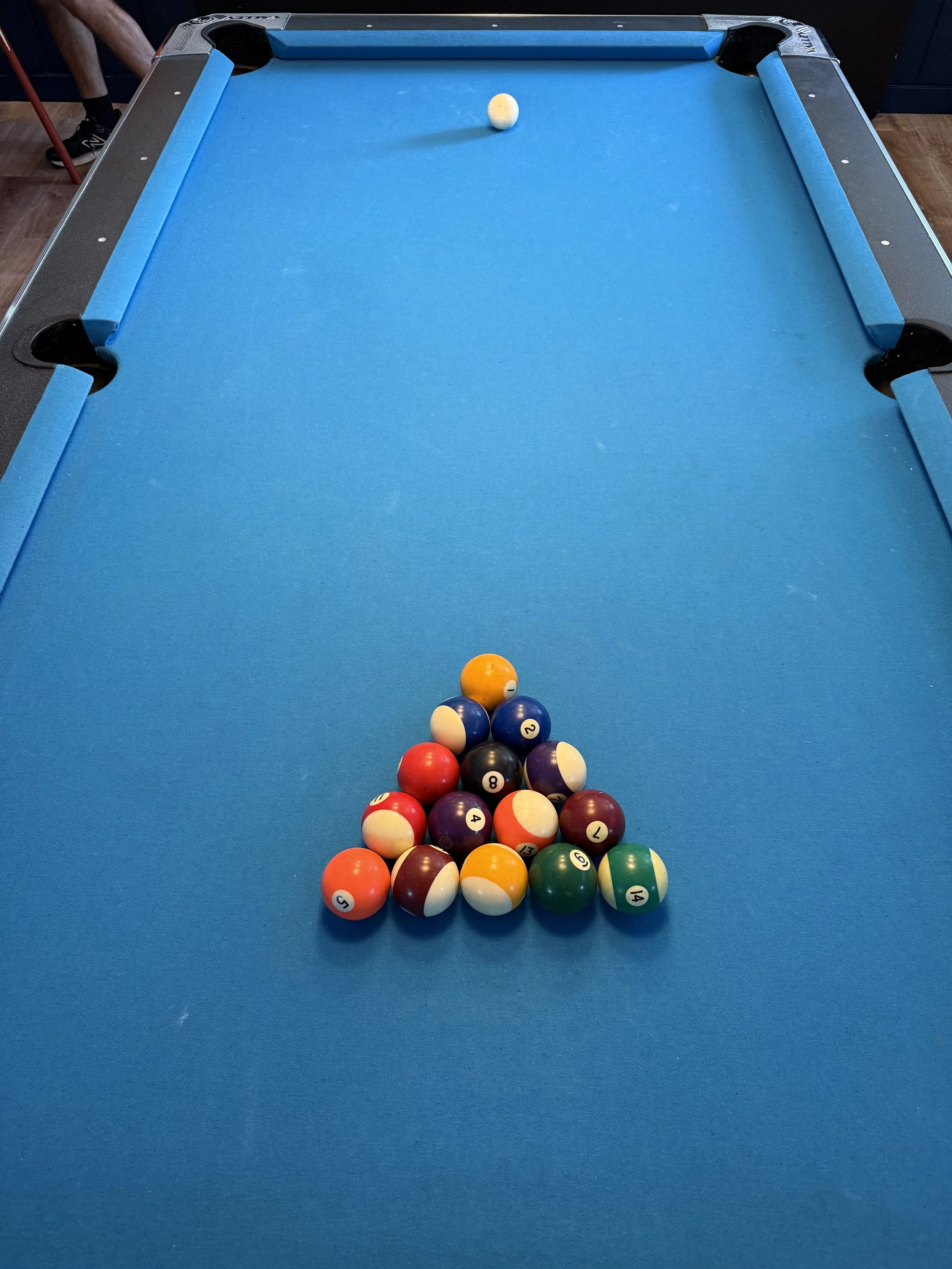 A pool table with a triangle of billiard balls arranged at the foot of the table, with the cue ball at the head.