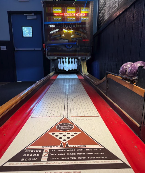 Vintage pinball machine with a bowling themed game, featuring a bowling lane and pins, set in a dark room with purple bowling balls on the right.