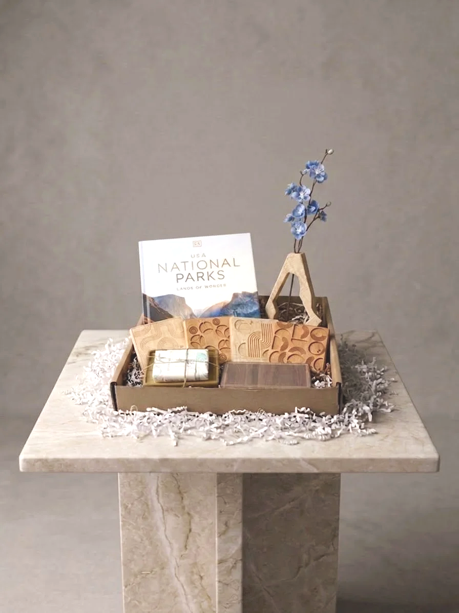 A display of various wooden and cardboard items, a miniature wooden easel with blue flowers, a small book titled 'National Parks,' and some decorative shredded paper on a light-colored marble table.