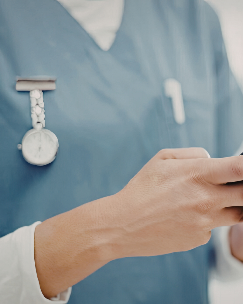Close-up of a medical professional wearing scrubs and a stethoscope looking at a mobile device.