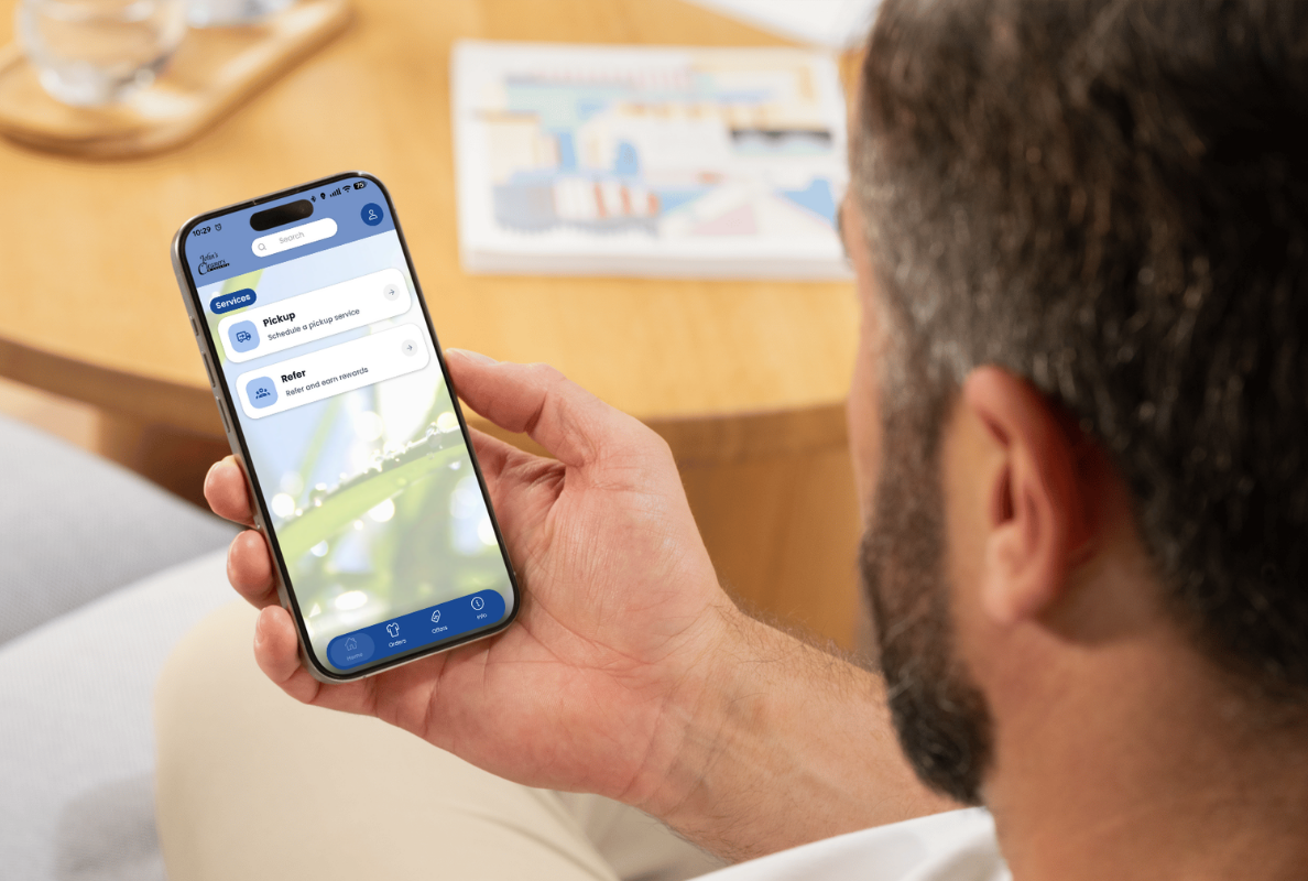 A person with dark hair and a beard looking at a smartphone with a transportation app open, showing 'Pickup' and 'Refer' options.